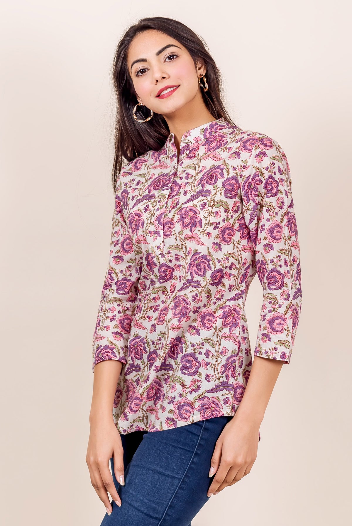 Smiling model wears off-white top with pink and purple floral print, 3/4 sleeves.