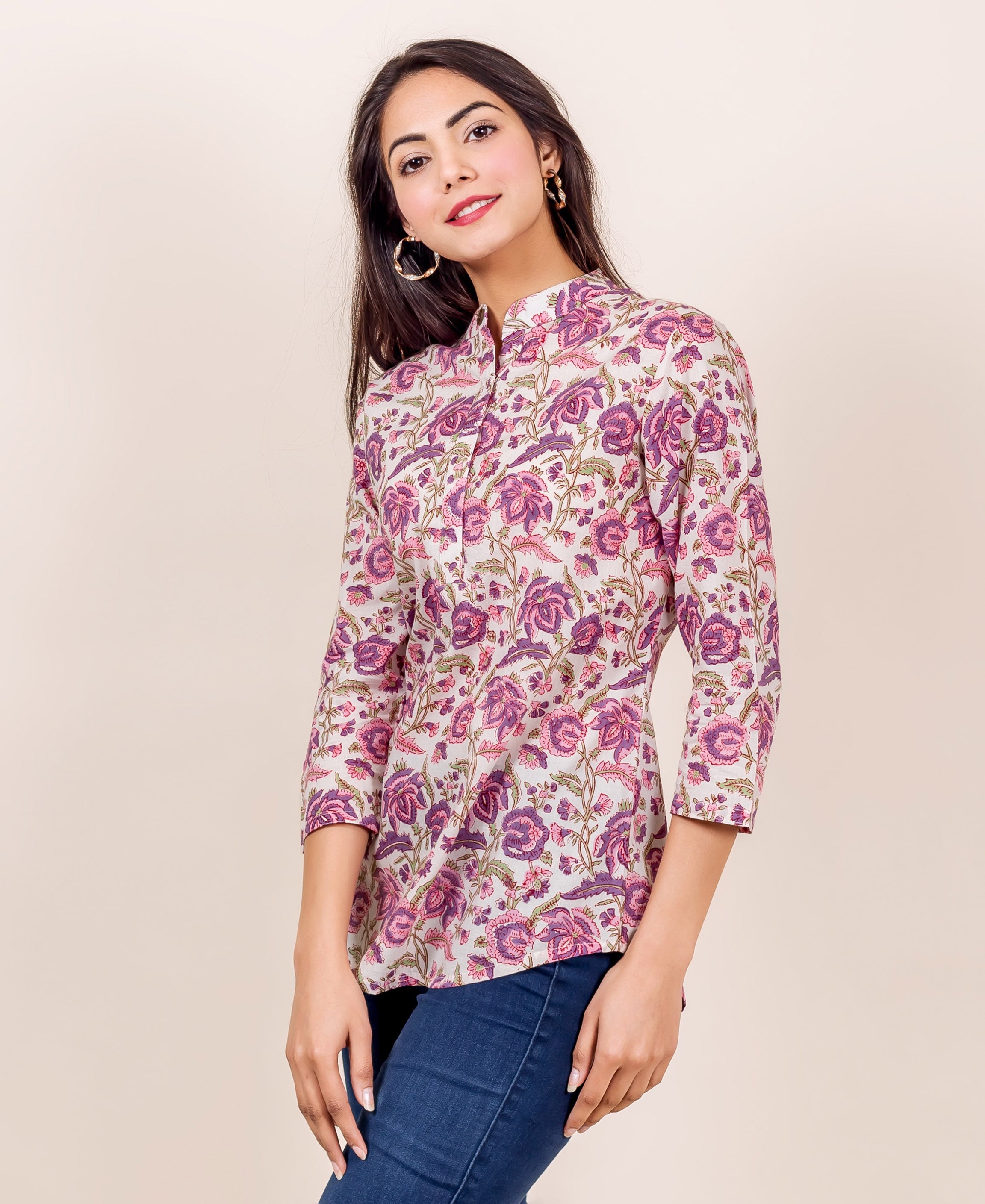 Smiling model wears off-white top with pink and purple floral print, 3/4 sleeves.