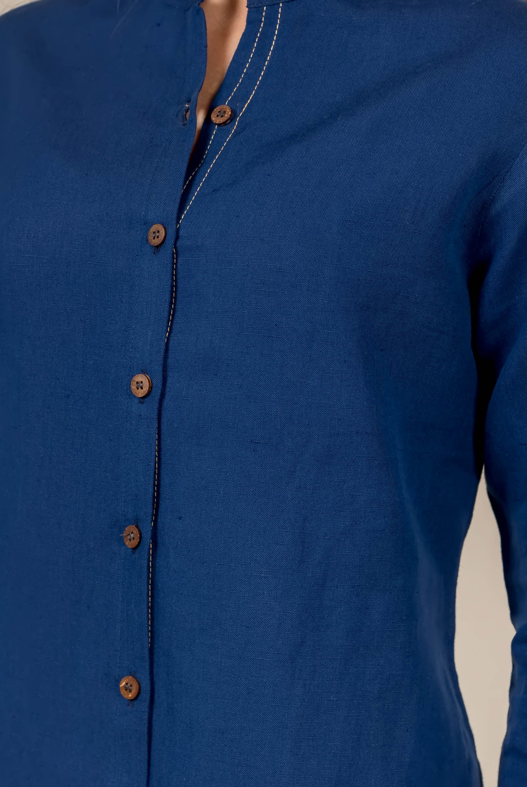Close-up of indigo blue linen button-down shirt on model, with wooden buttons and stitch details.