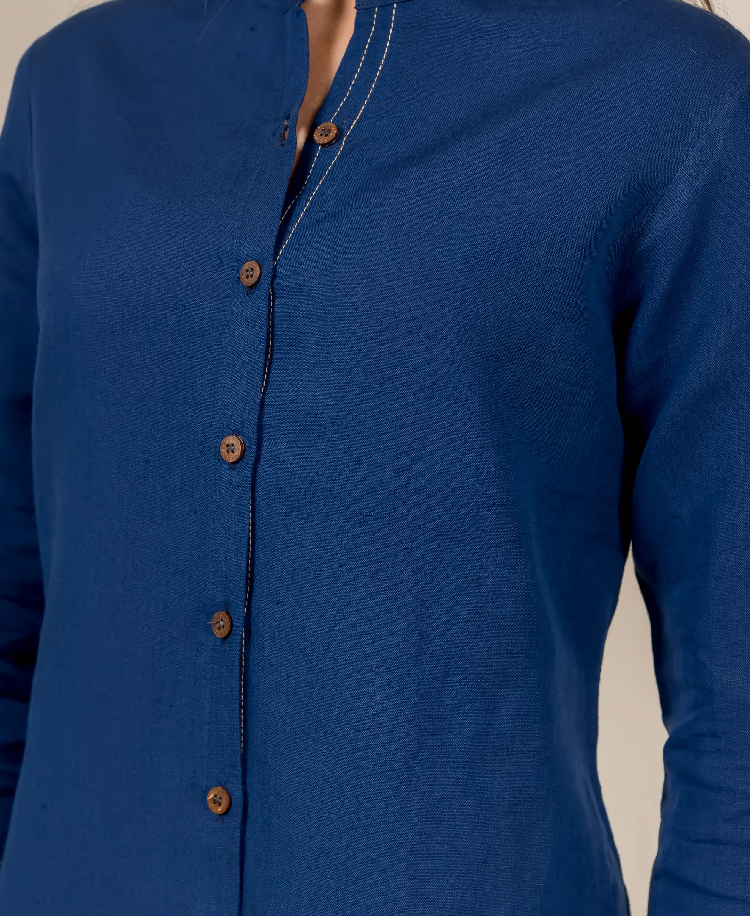 Close-up of indigo blue linen button-down shirt on model, with wooden buttons and stitch details.