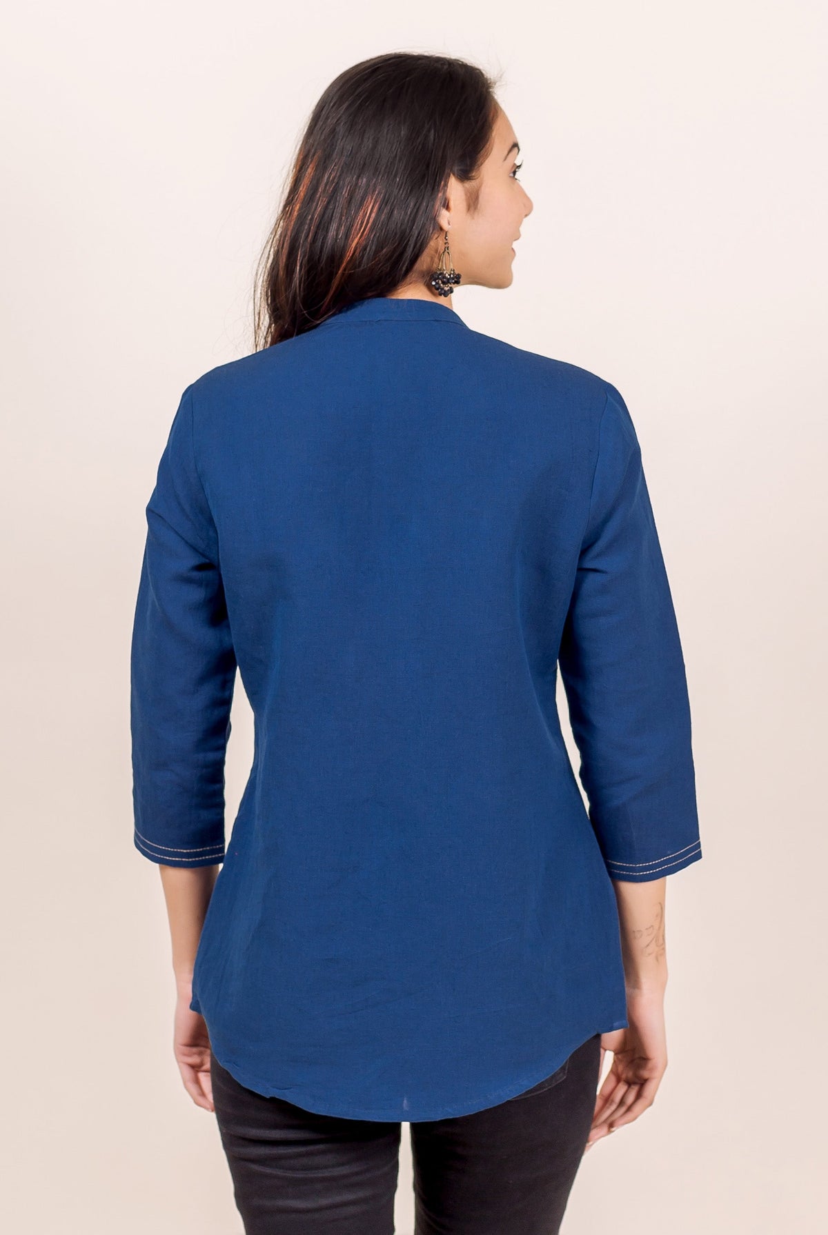 Woman from back wearing an indigo blue linen shirt with 3/4 sleeves and curved hem.