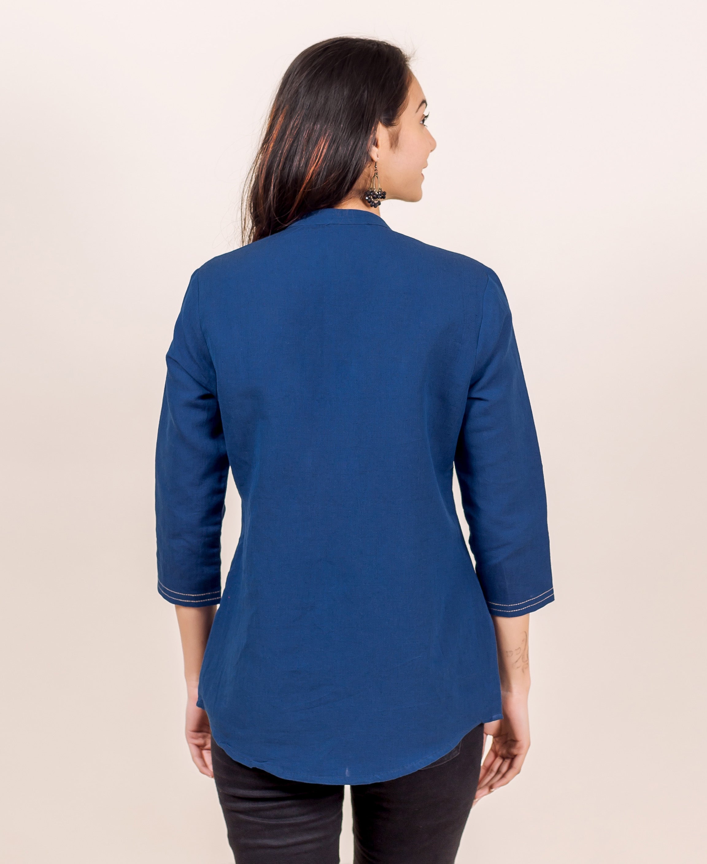 Woman from back wearing an indigo blue linen shirt with 3/4 sleeves and curved hem.