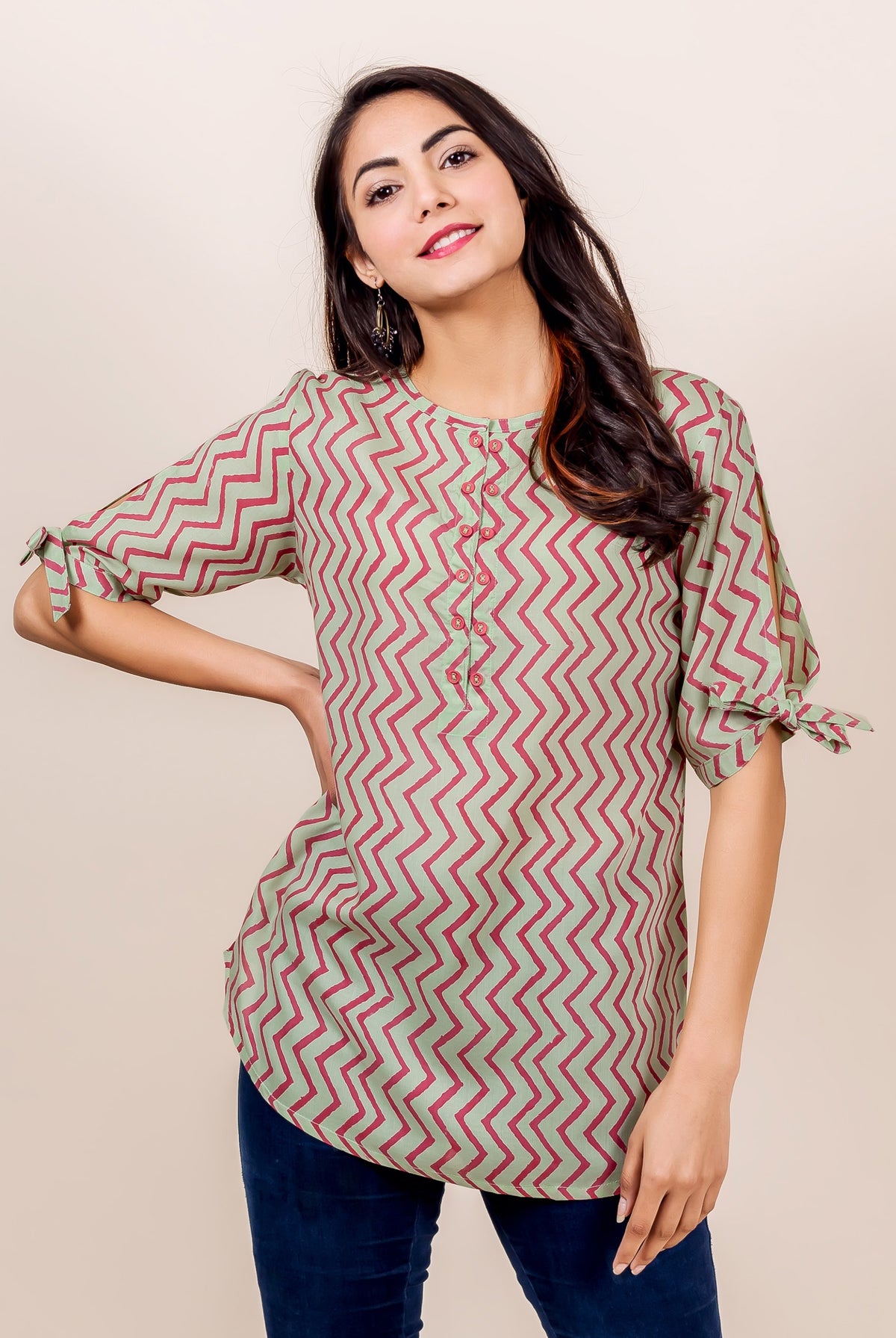 Woman wearing mint green and pink zigzag patterned top with short sleeves and blue jeans.