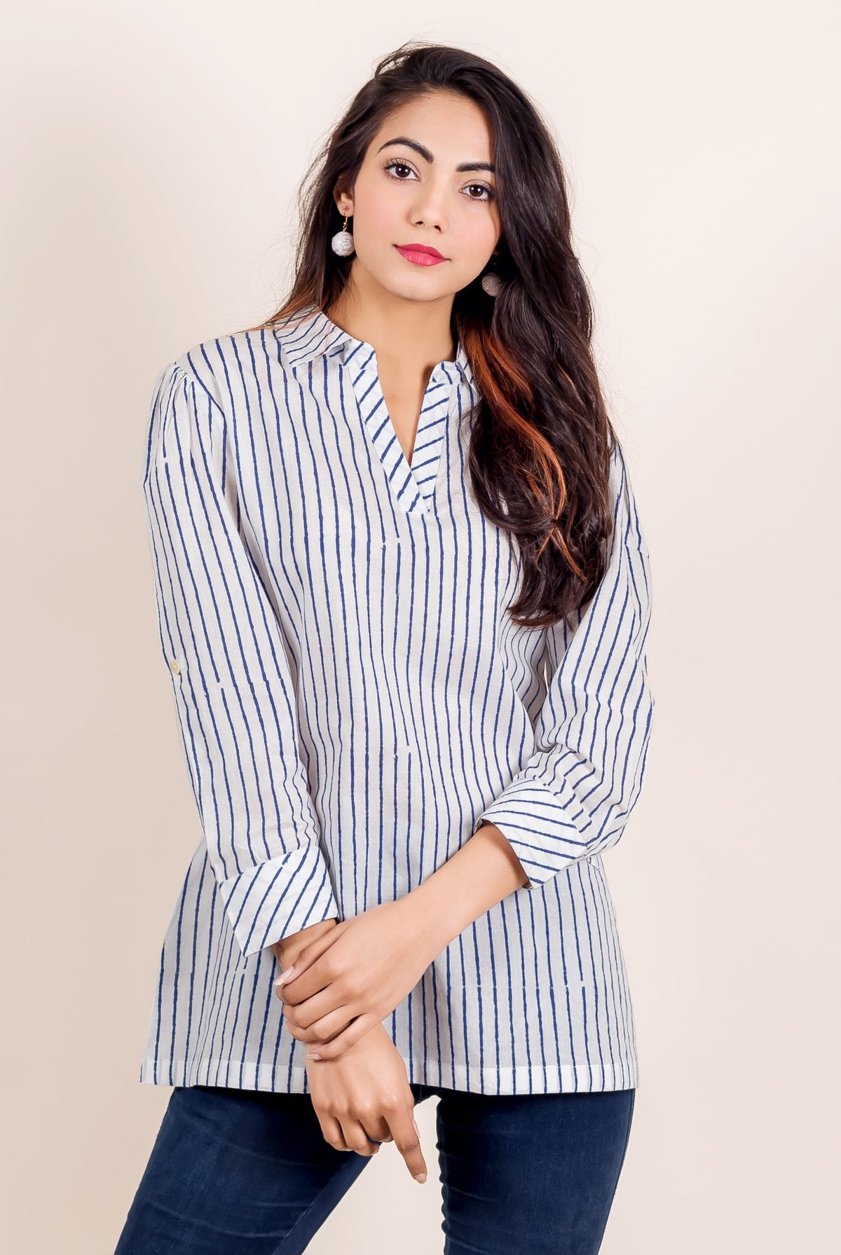 Woman models white and blue uneven striped V-neck tunic top with dark jeans.
