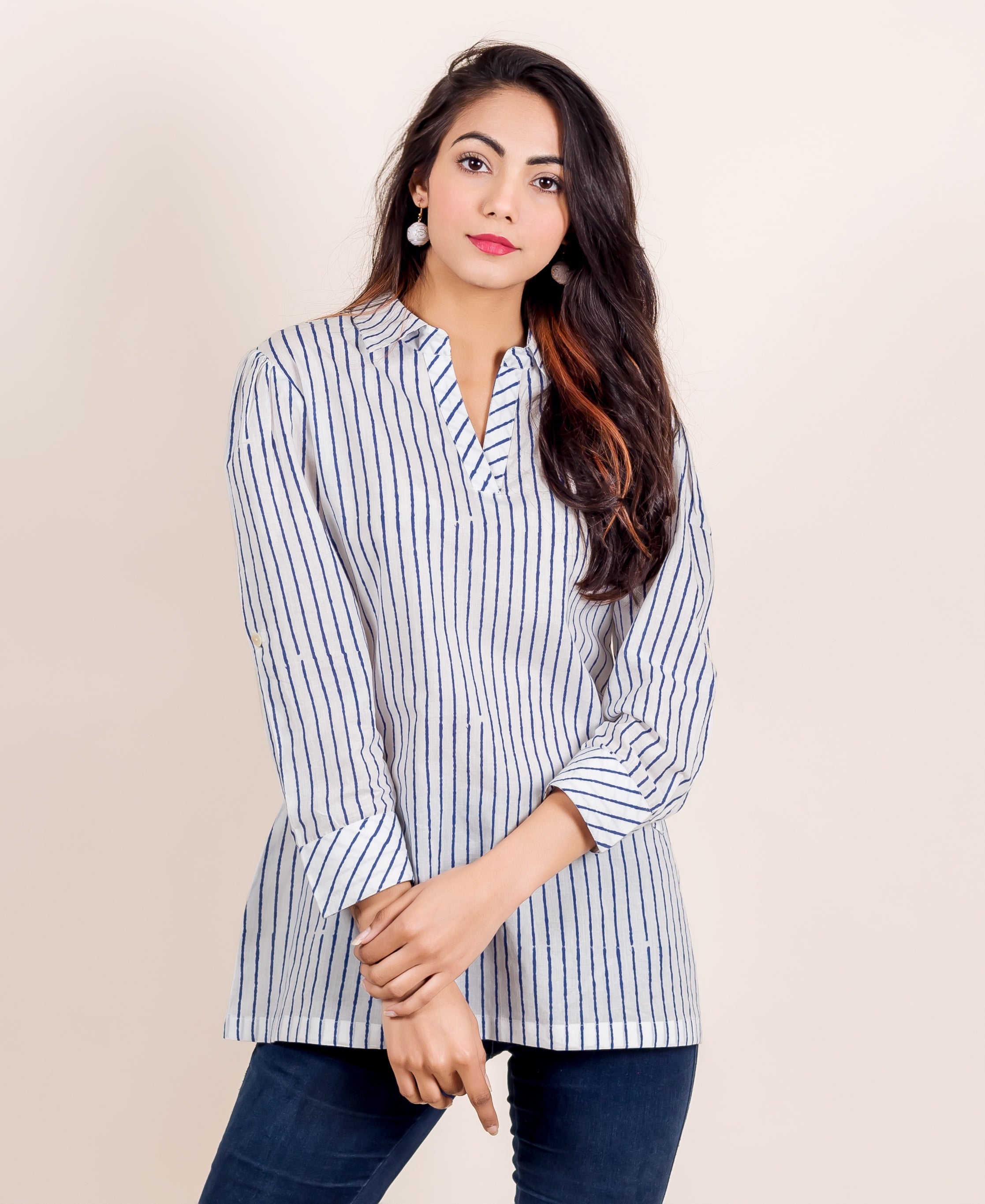 Woman models white and blue uneven striped V-neck tunic top with dark jeans.