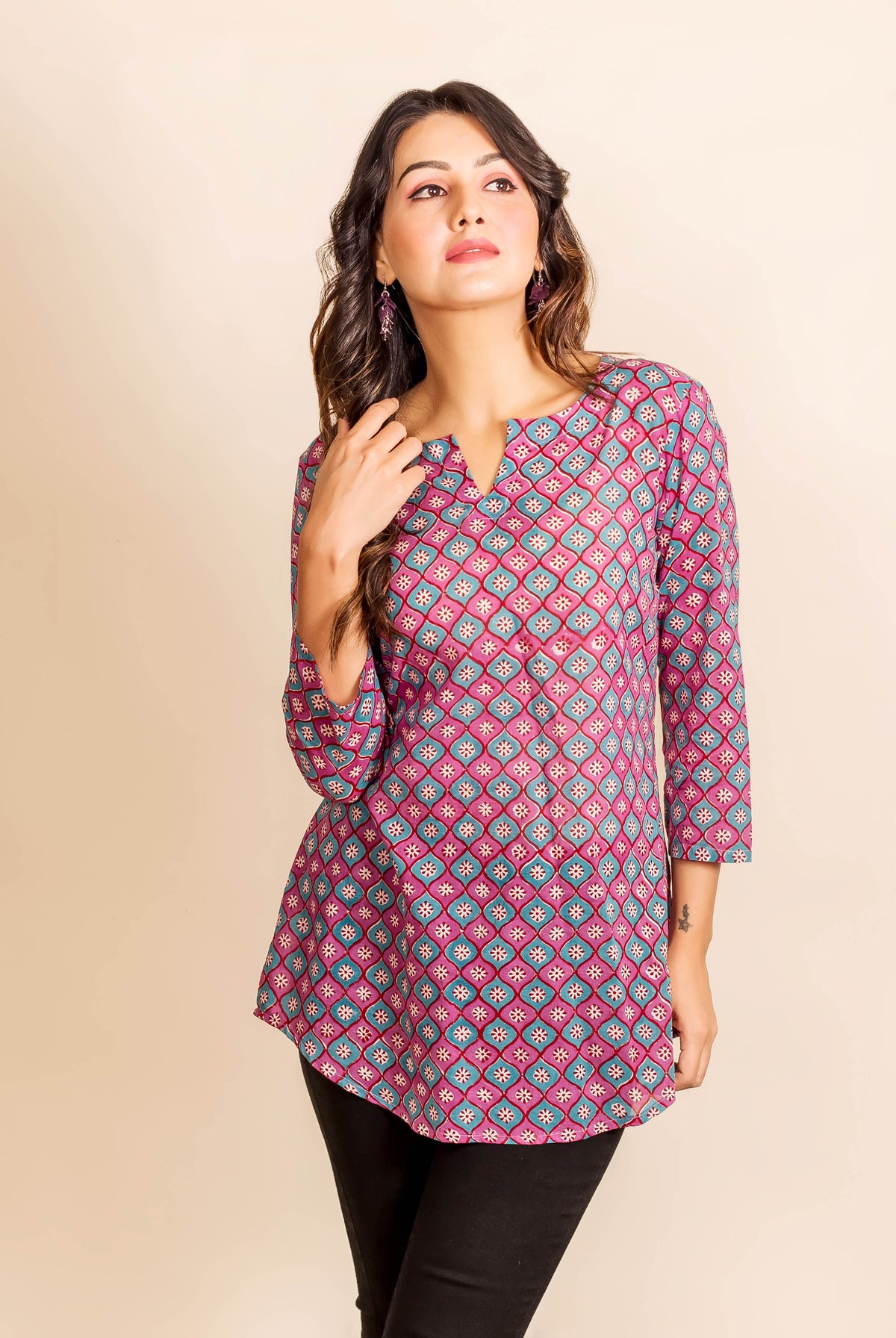 Woman in a three-quarter shot wearing a magenta and teal geometric block print tunic top.