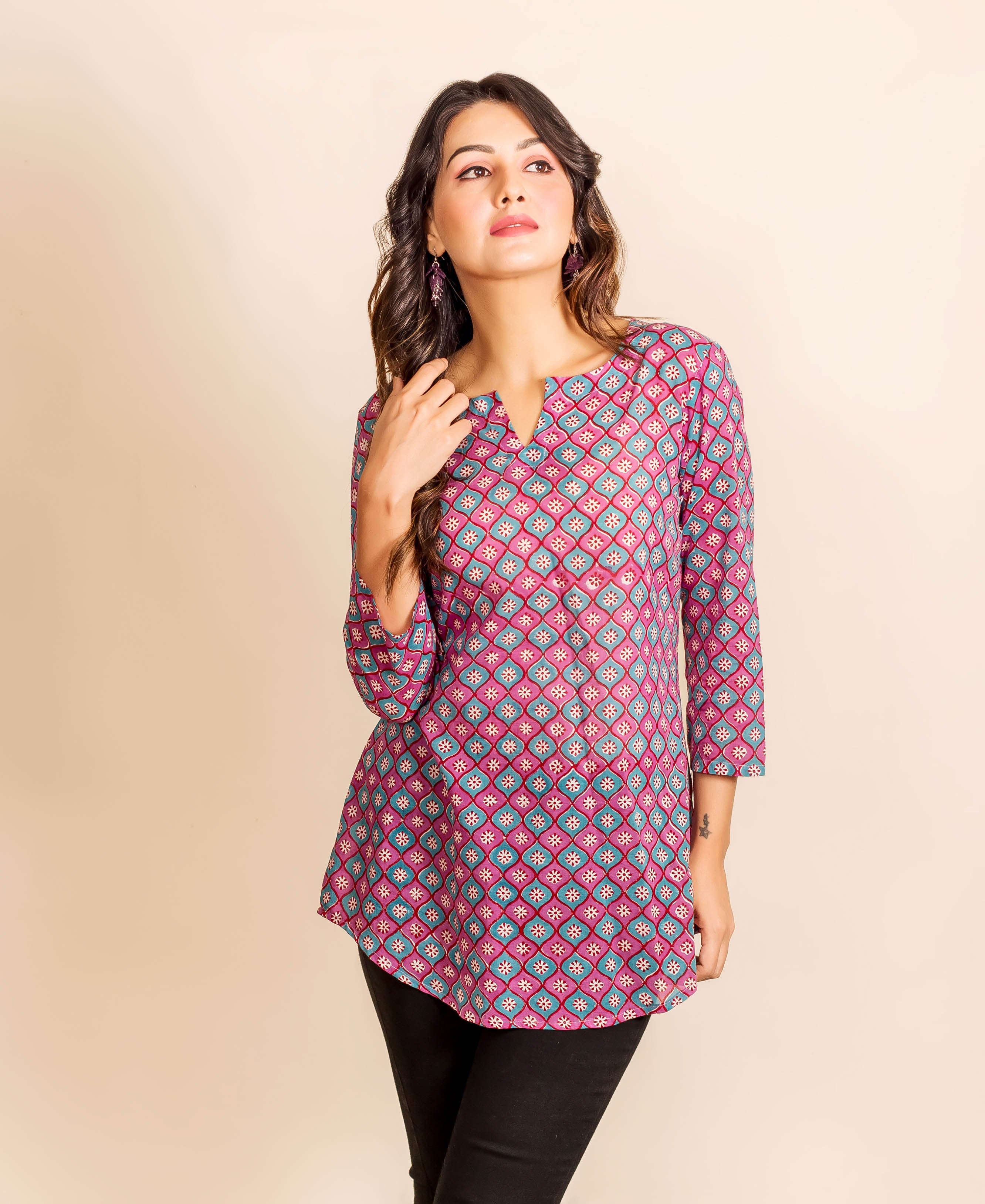 Woman in a three-quarter shot wearing a magenta and teal geometric block print tunic top.