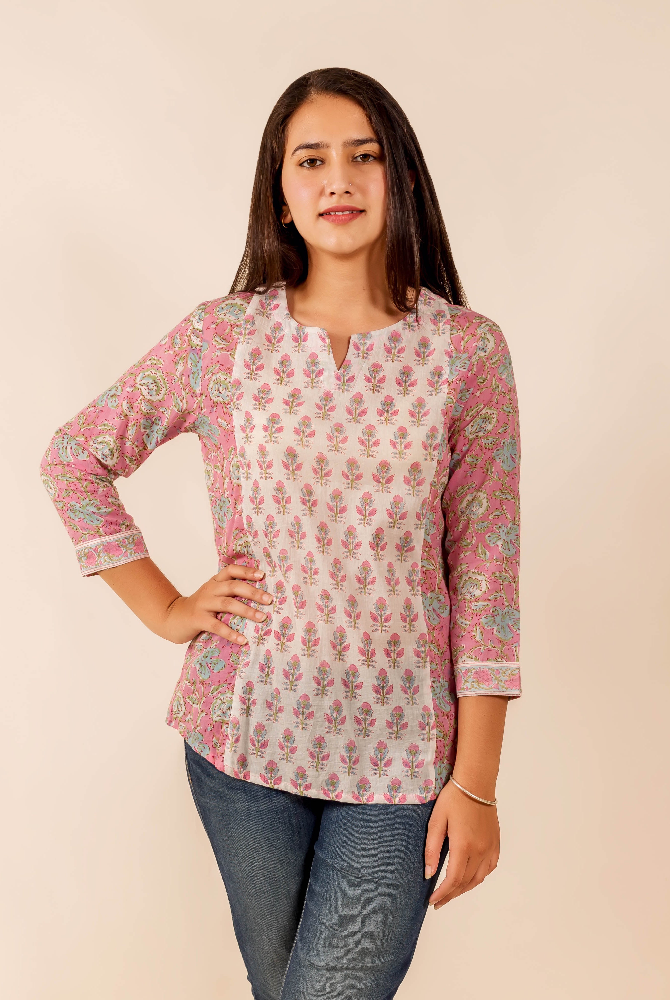 Woman models a pink and white hand block printed floral top, standing front.