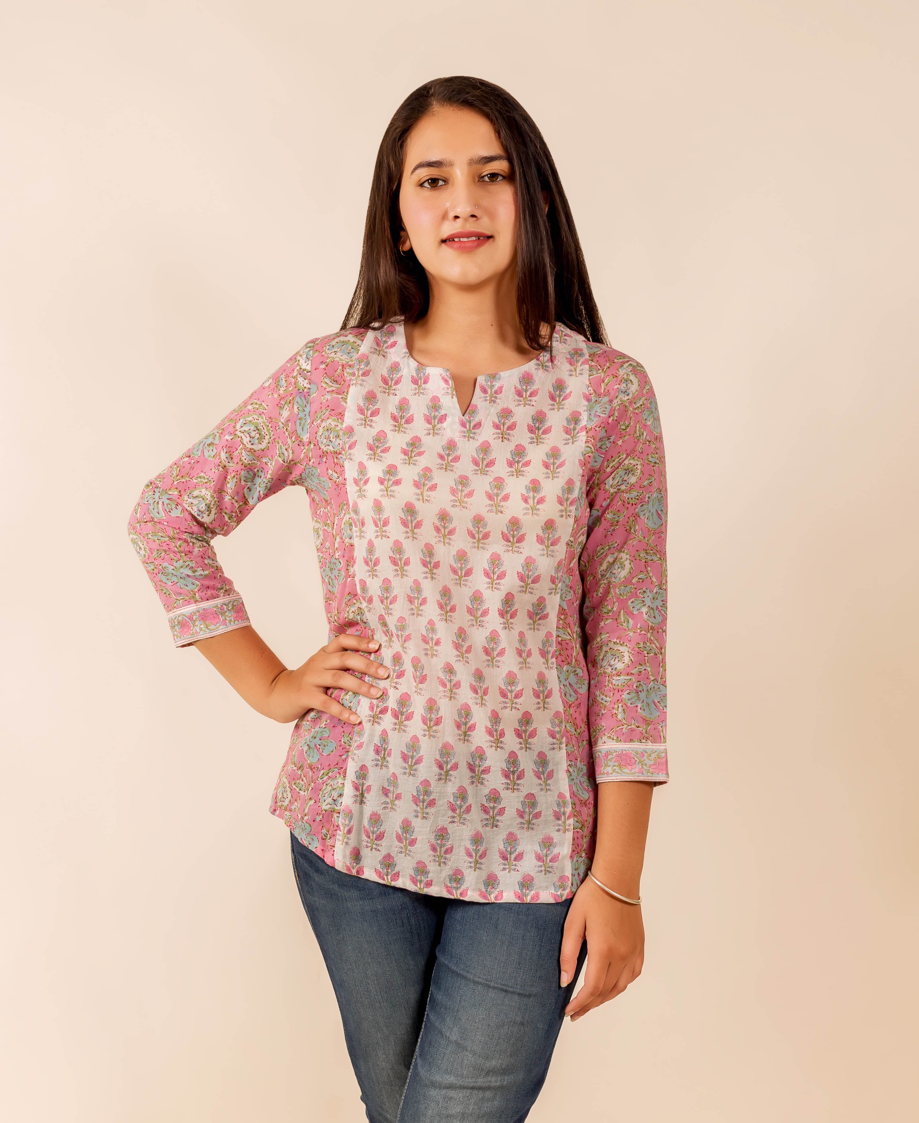 Woman models a pink and white hand block printed floral top, standing front.