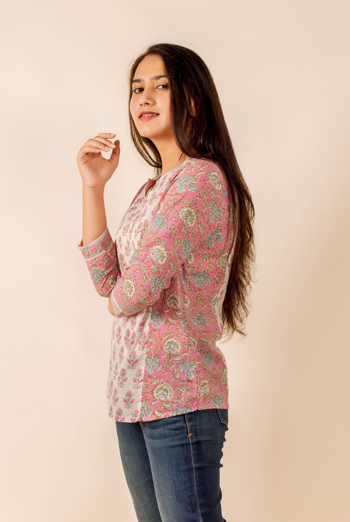 Young woman in a pink and white hand-block printed floral top and blue jeans, side view.
