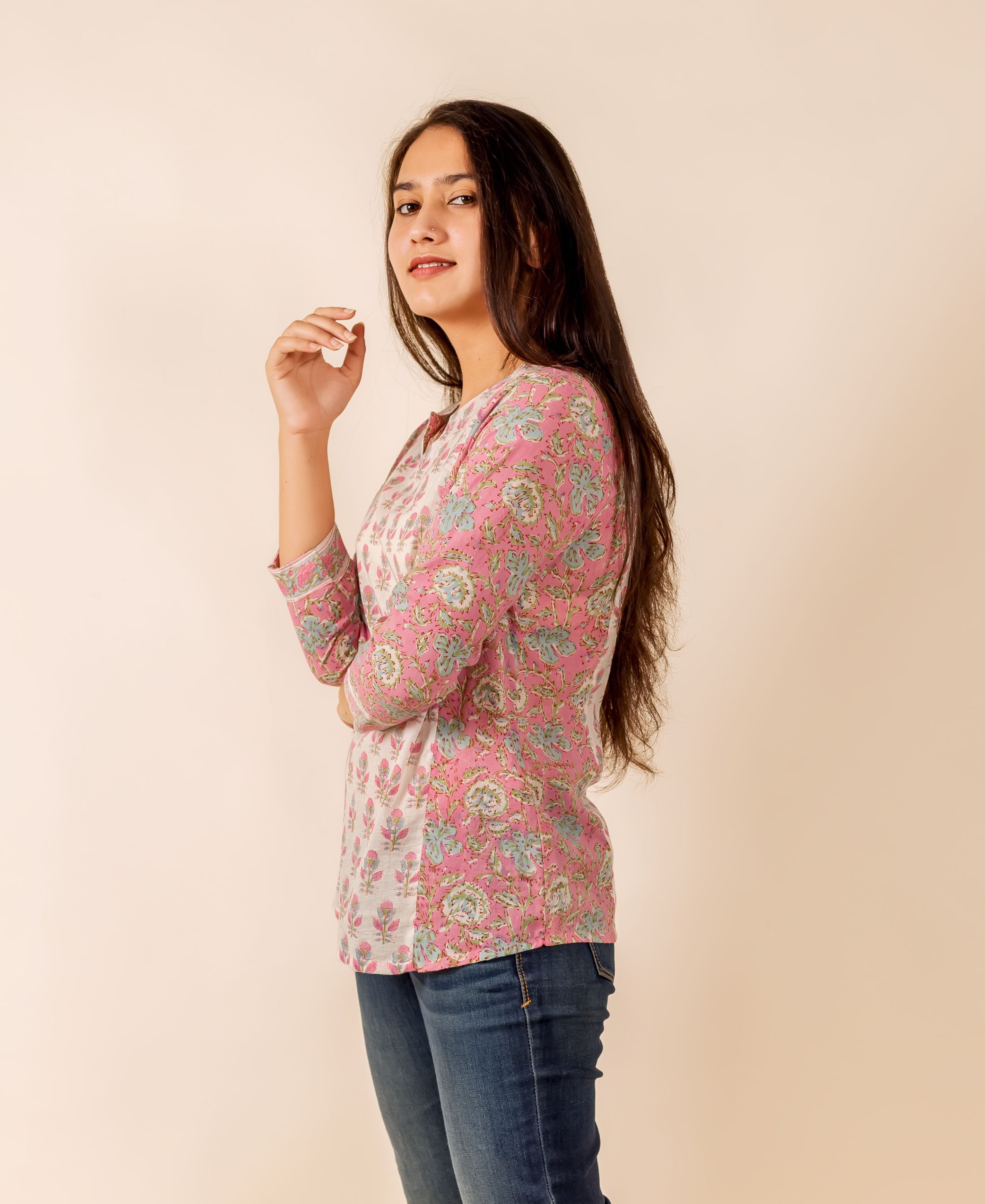 Young woman in a pink and white hand-block printed floral top and blue jeans, side view.