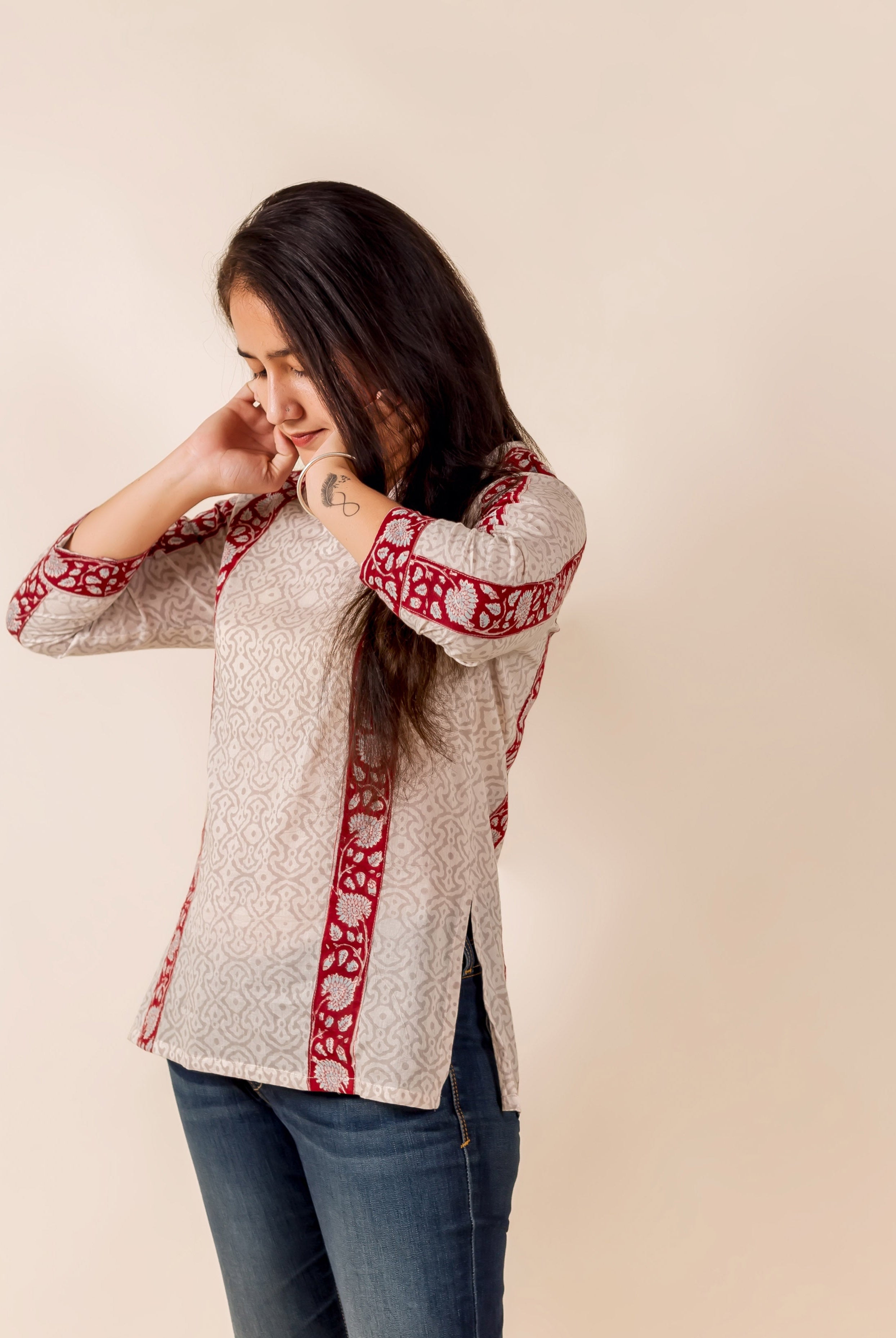 Woman in off-white hand-block-printed top with maroon ethnic borders, paired with blue jeans.