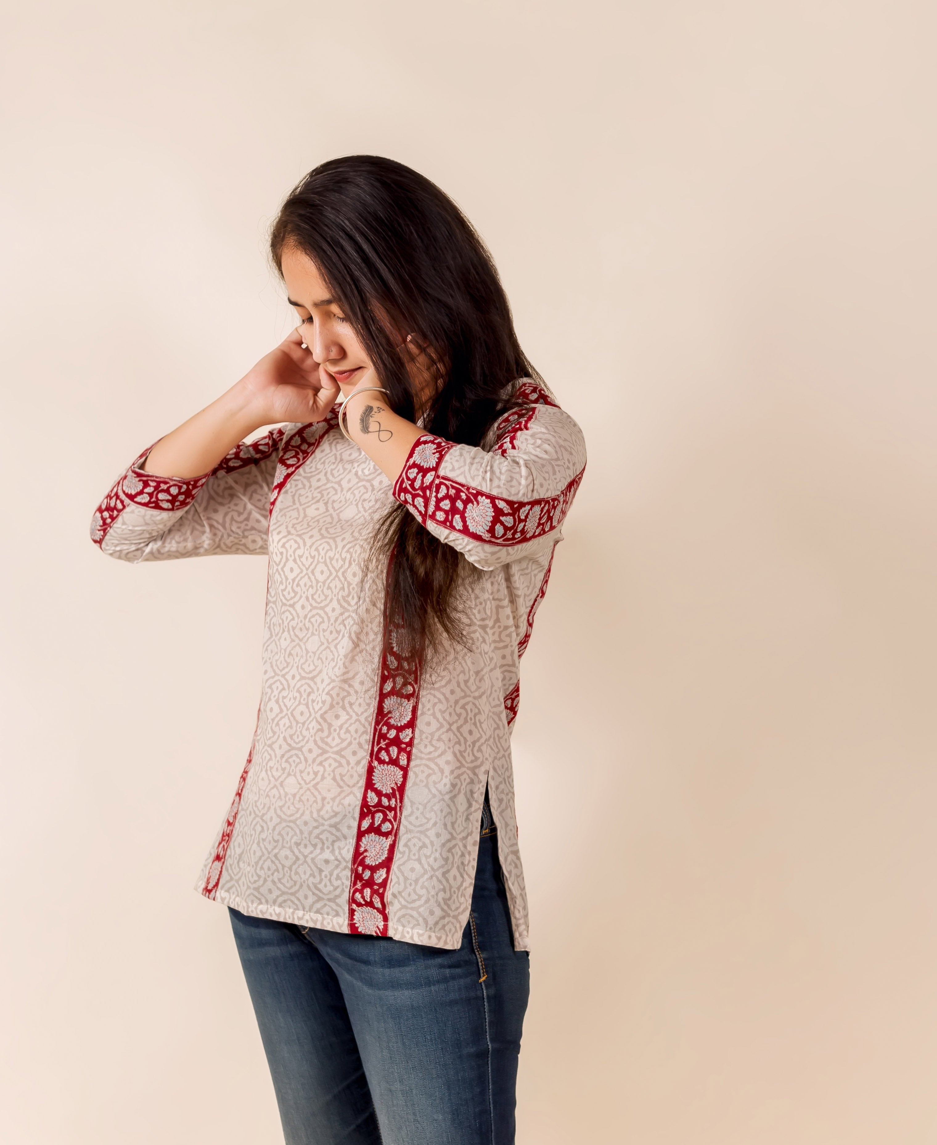 Woman in off-white hand-block-printed top with maroon ethnic borders, paired with blue jeans.