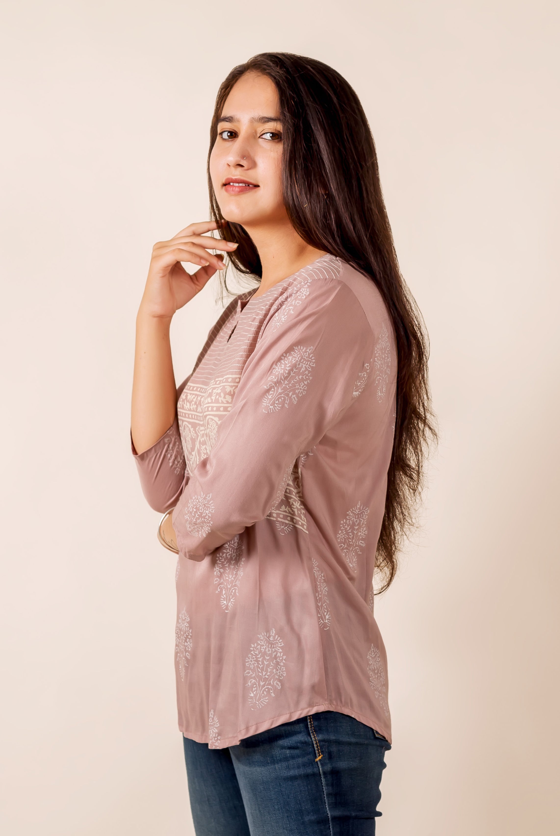 Side view of model in dusty pink top with white ethnic prints and blue jeans.