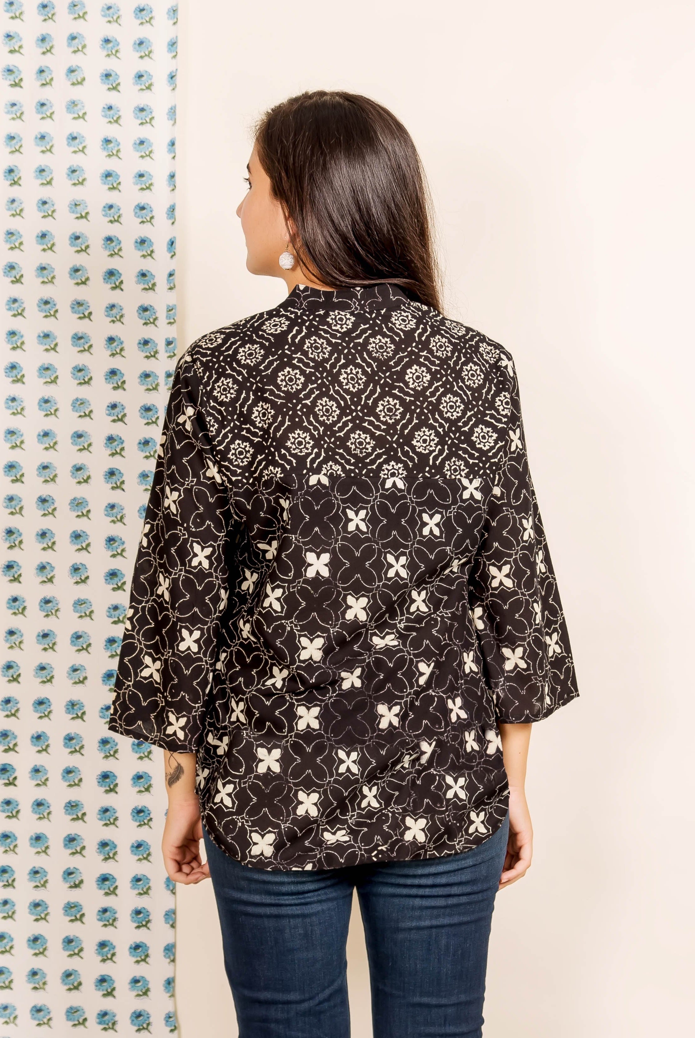 Rear view of model in black hand-block printed top with white geometric and floral patterns.