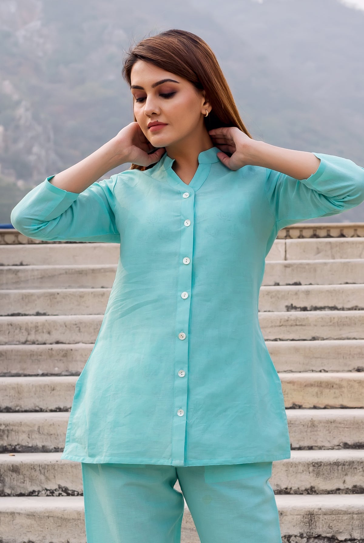 Front view of a model wearing a plain light aqua linen button-down top.