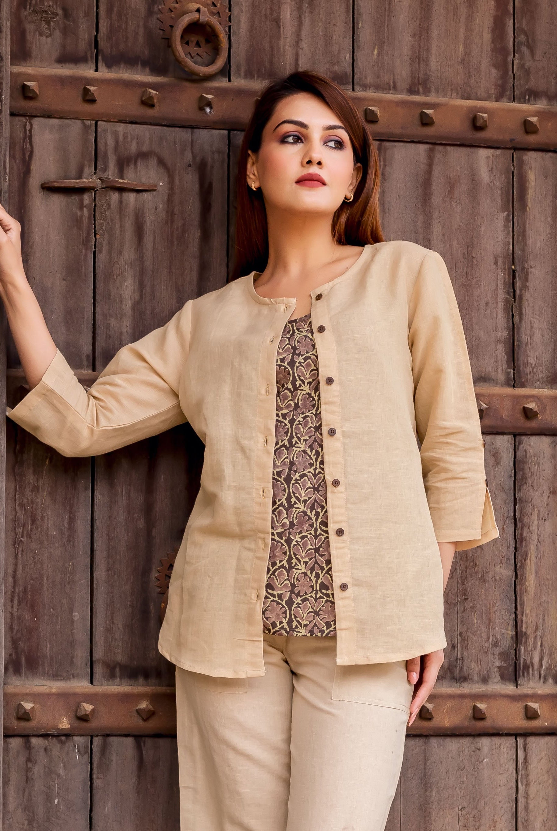 Beige linen button-down top on model, revealing dark ethnic floral print undershirt.