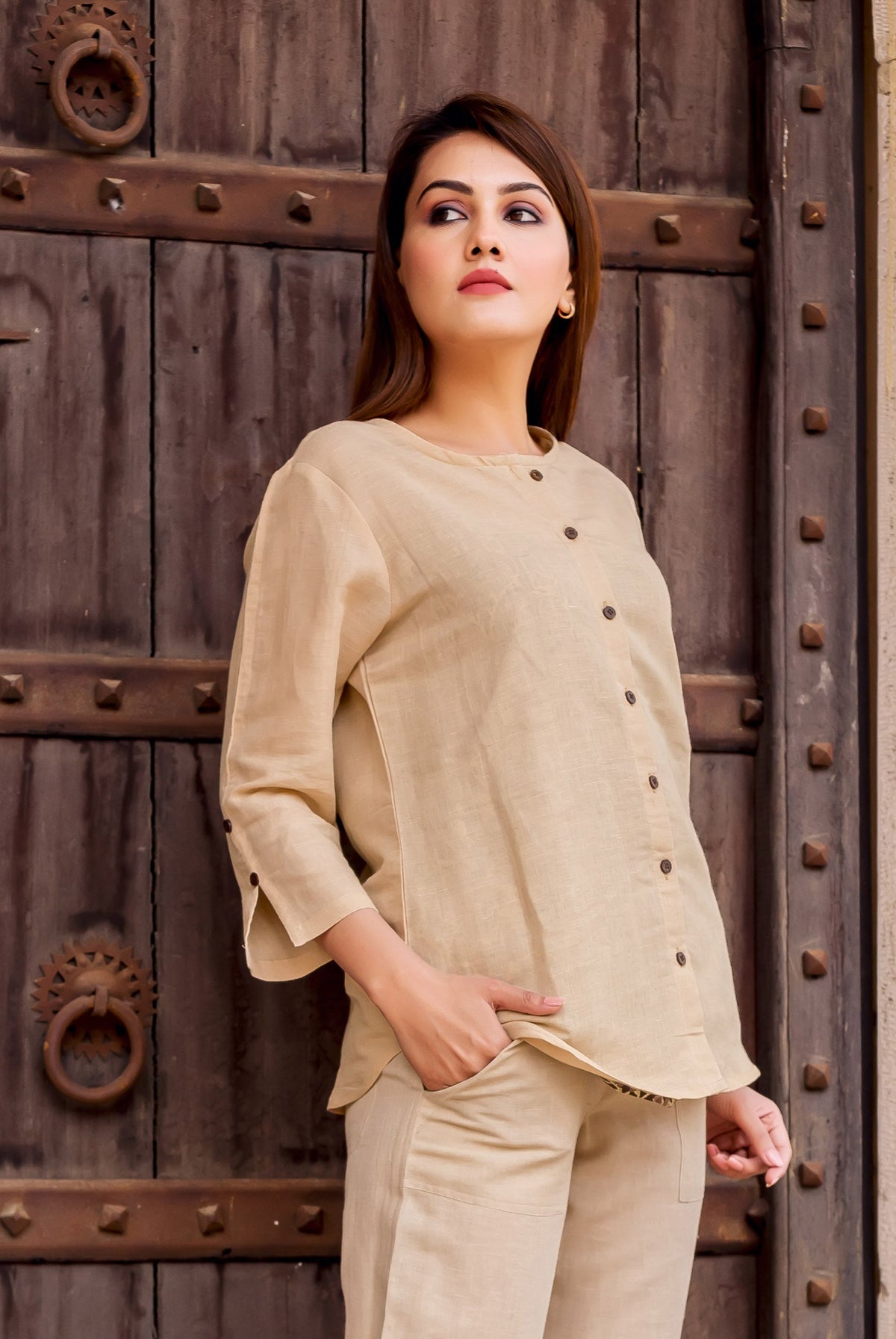 Model wears plain beige linen button-down top with round neck and three-quarter sleeves.
