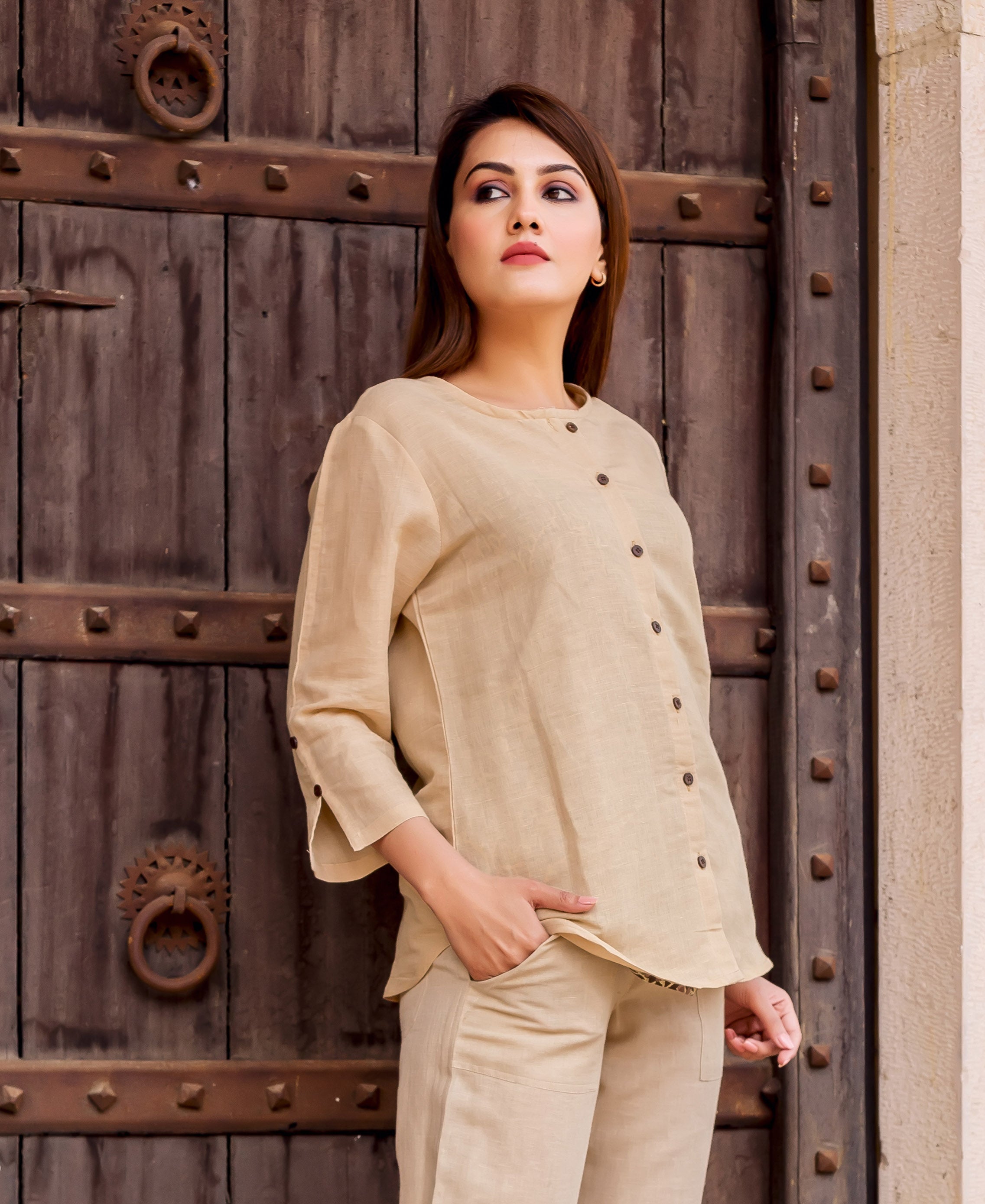 Model wears plain beige linen button-down top with round neck and three-quarter sleeves.
