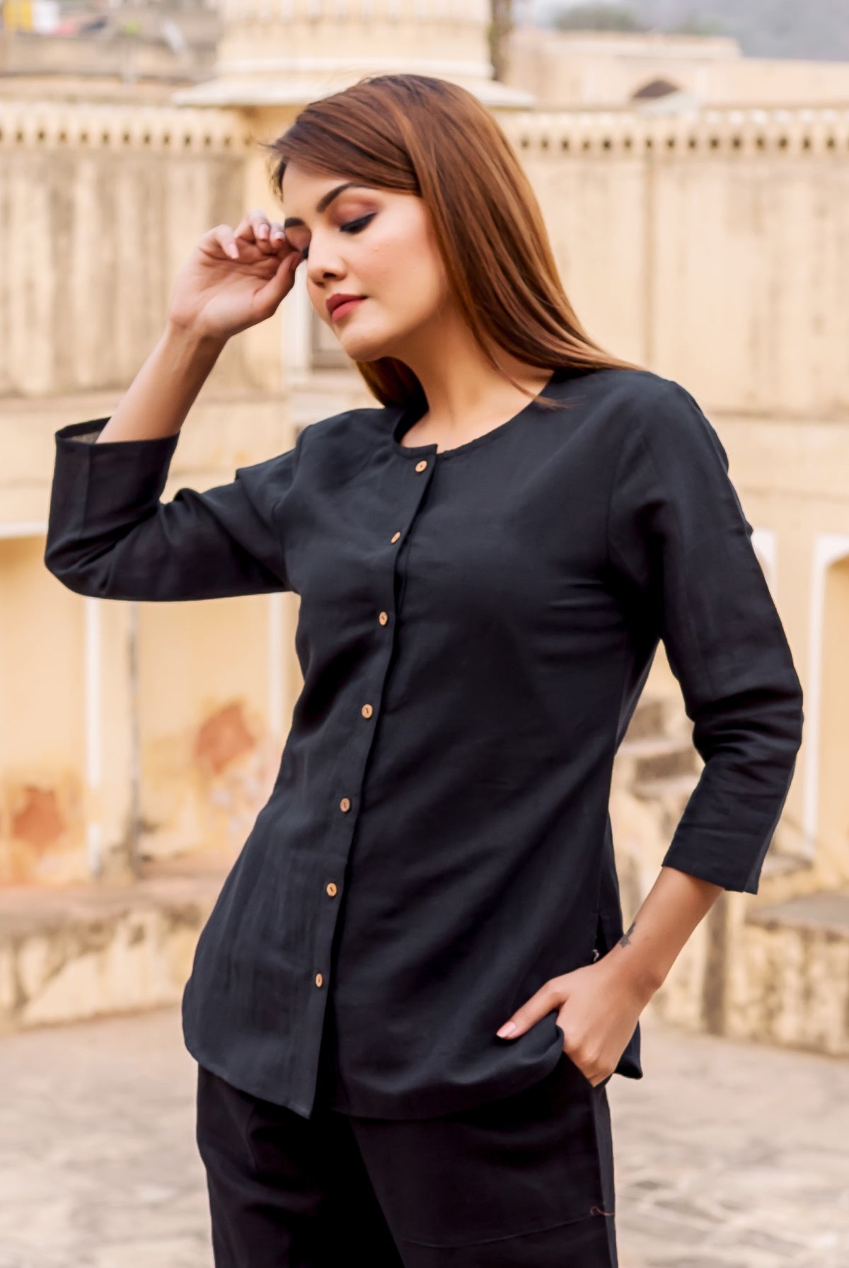Front view of model in black linen button-down top with round neck and wooden buttons.
