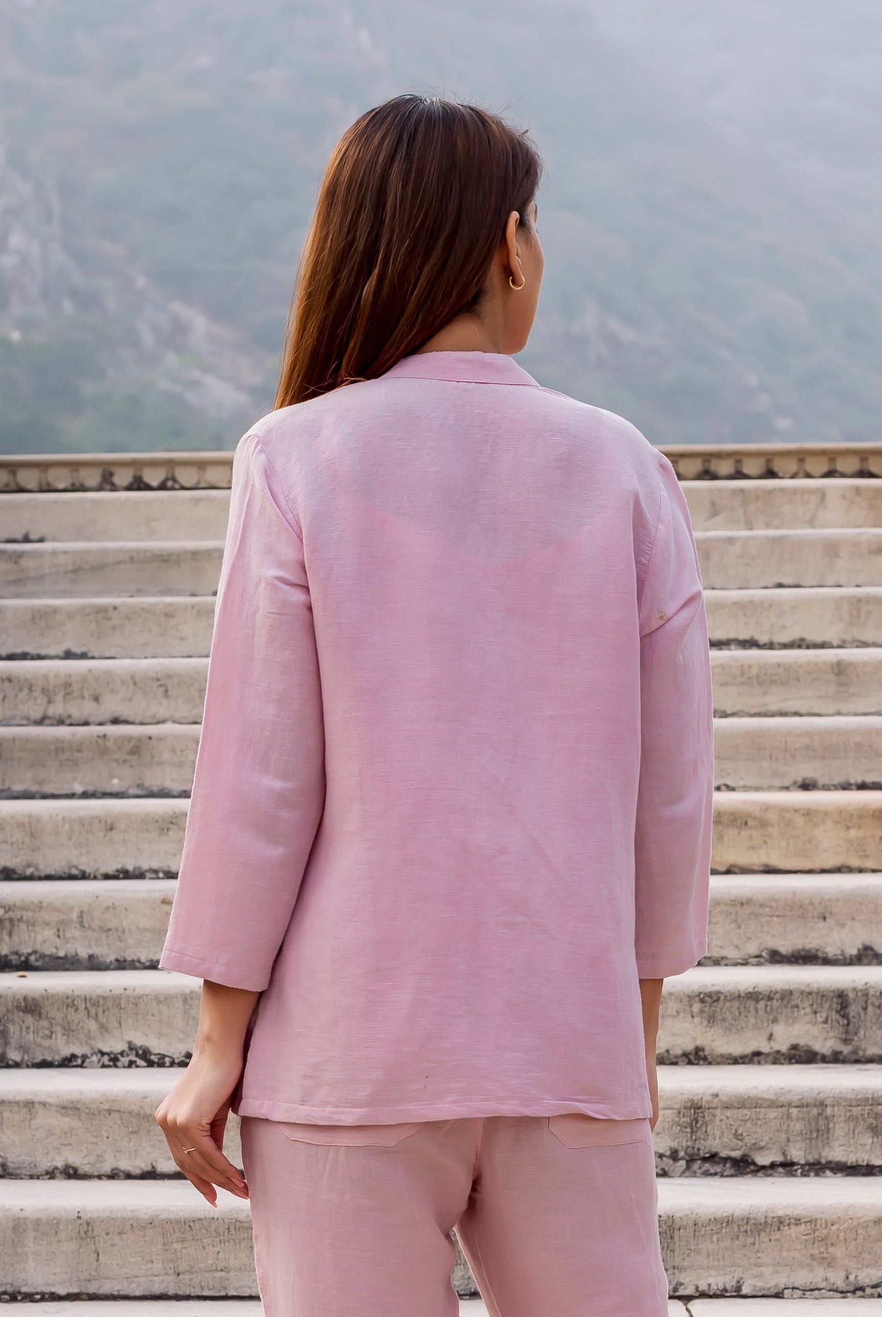 Back view of model in a flamingo pink linen top and matching pants on outdoor stairs.
