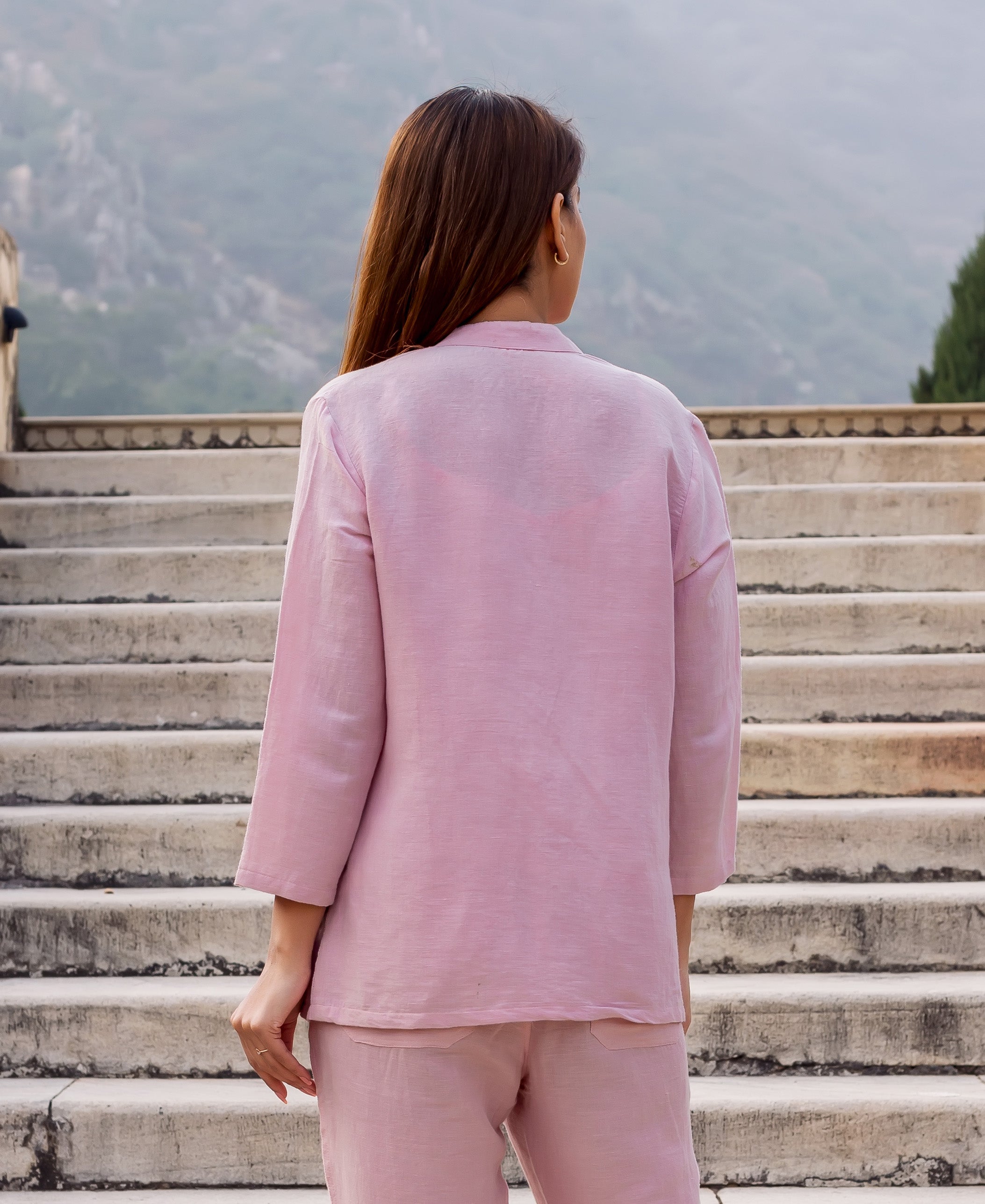 Back view of model in a flamingo pink linen top and matching pants on outdoor stairs.