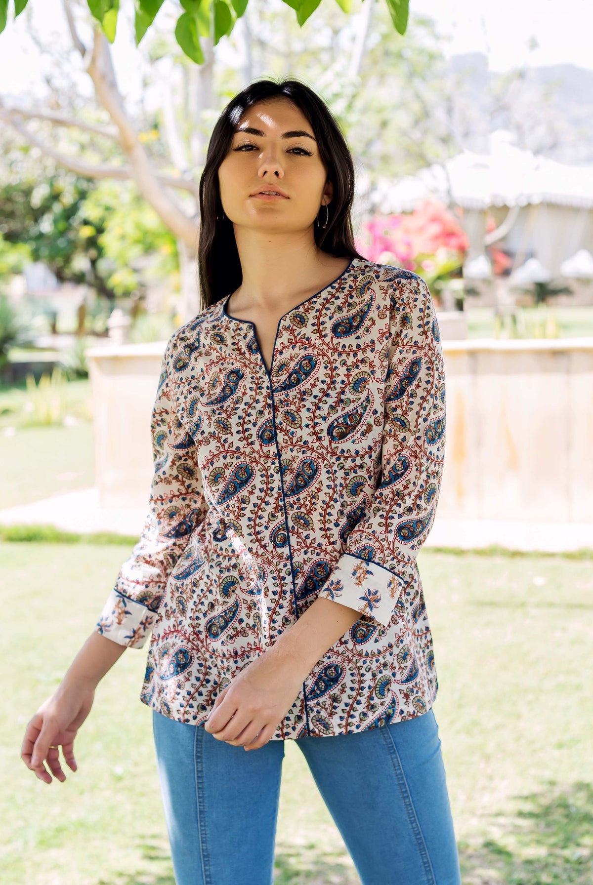 Woman models white paisley printed top with blue accents, split neckline, and rolled sleeves.