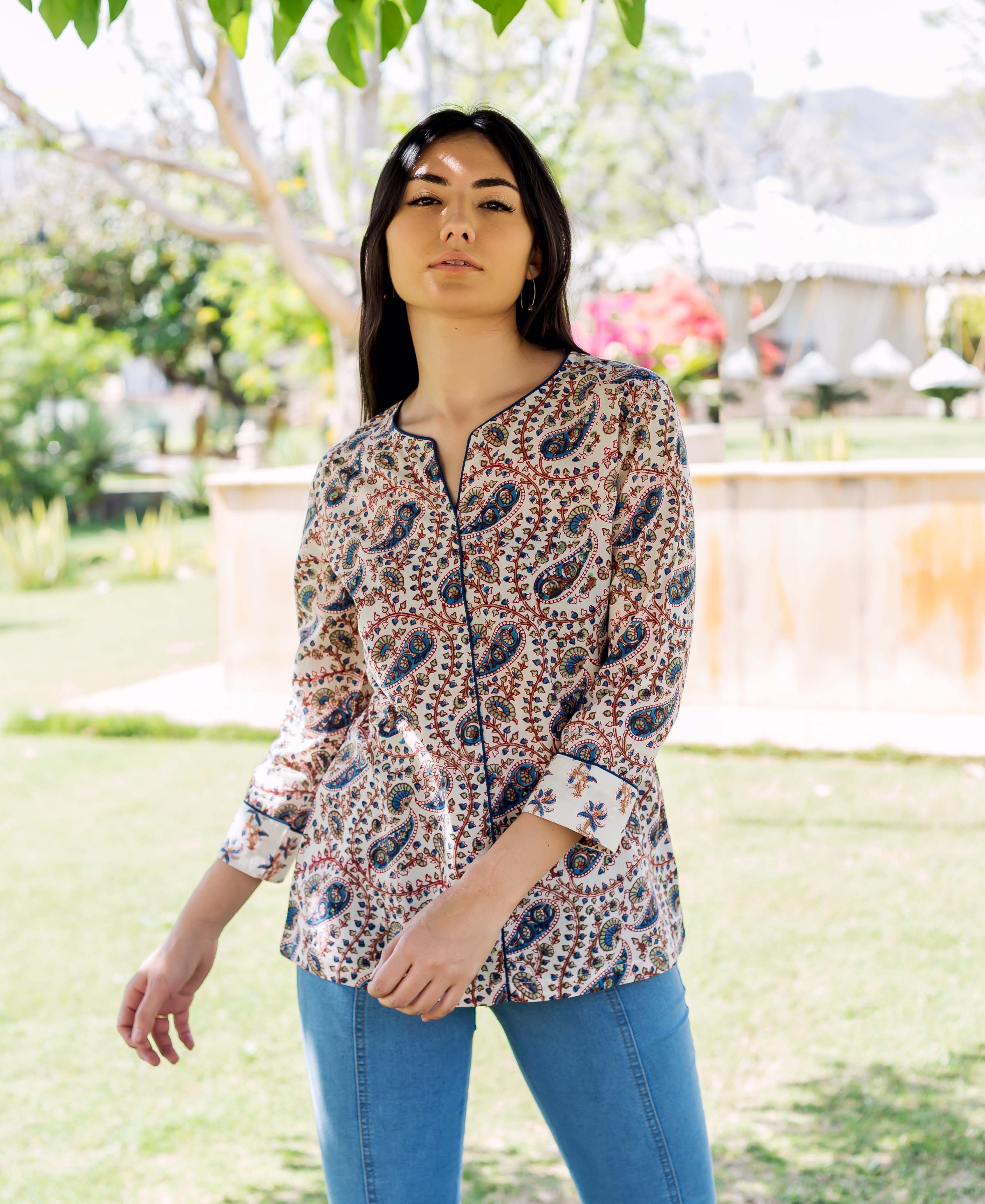 Woman models white paisley printed top with blue accents, split neckline, and rolled sleeves.