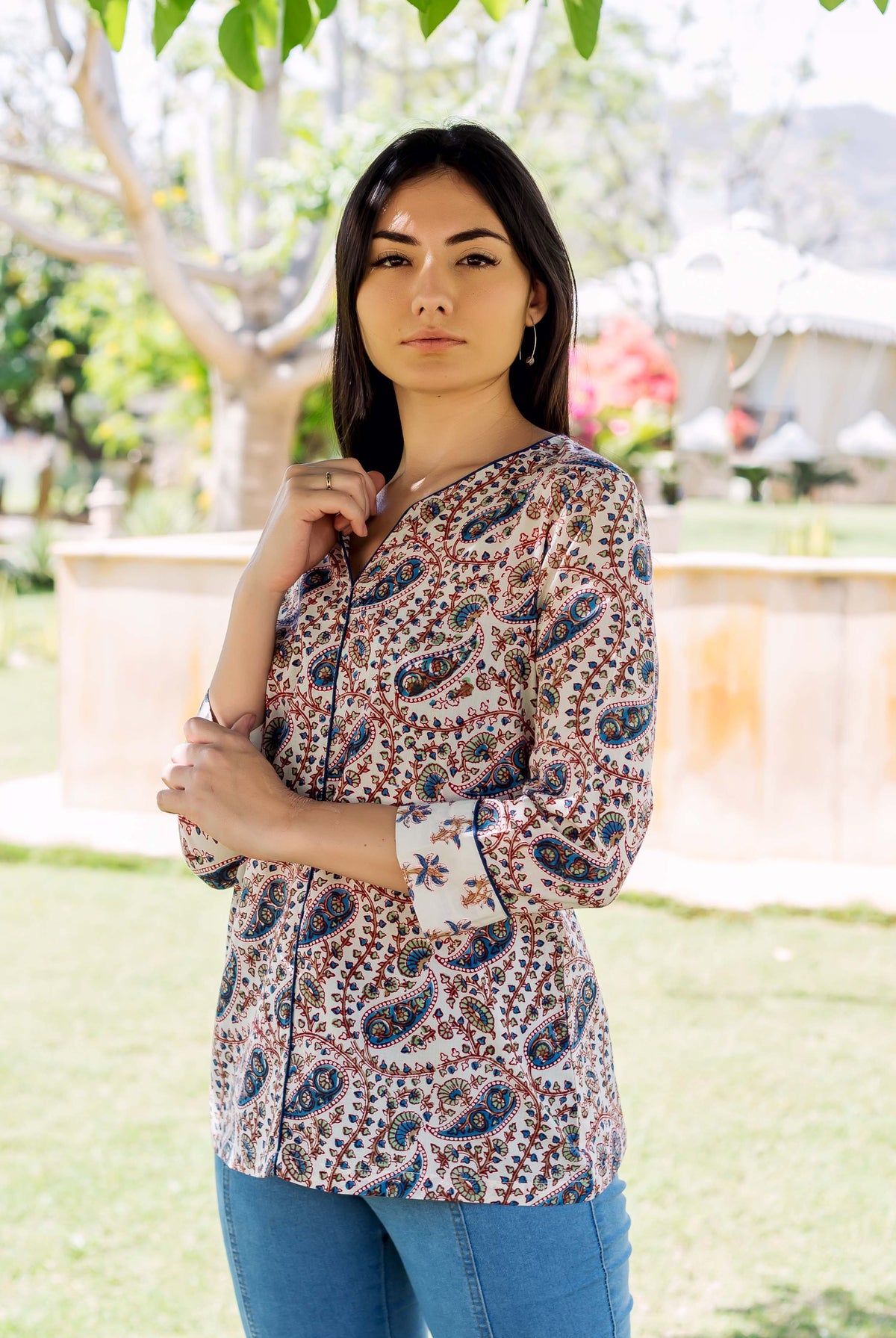 Model wearing a white button-down top with intricate blue and red paisley print outdoors.