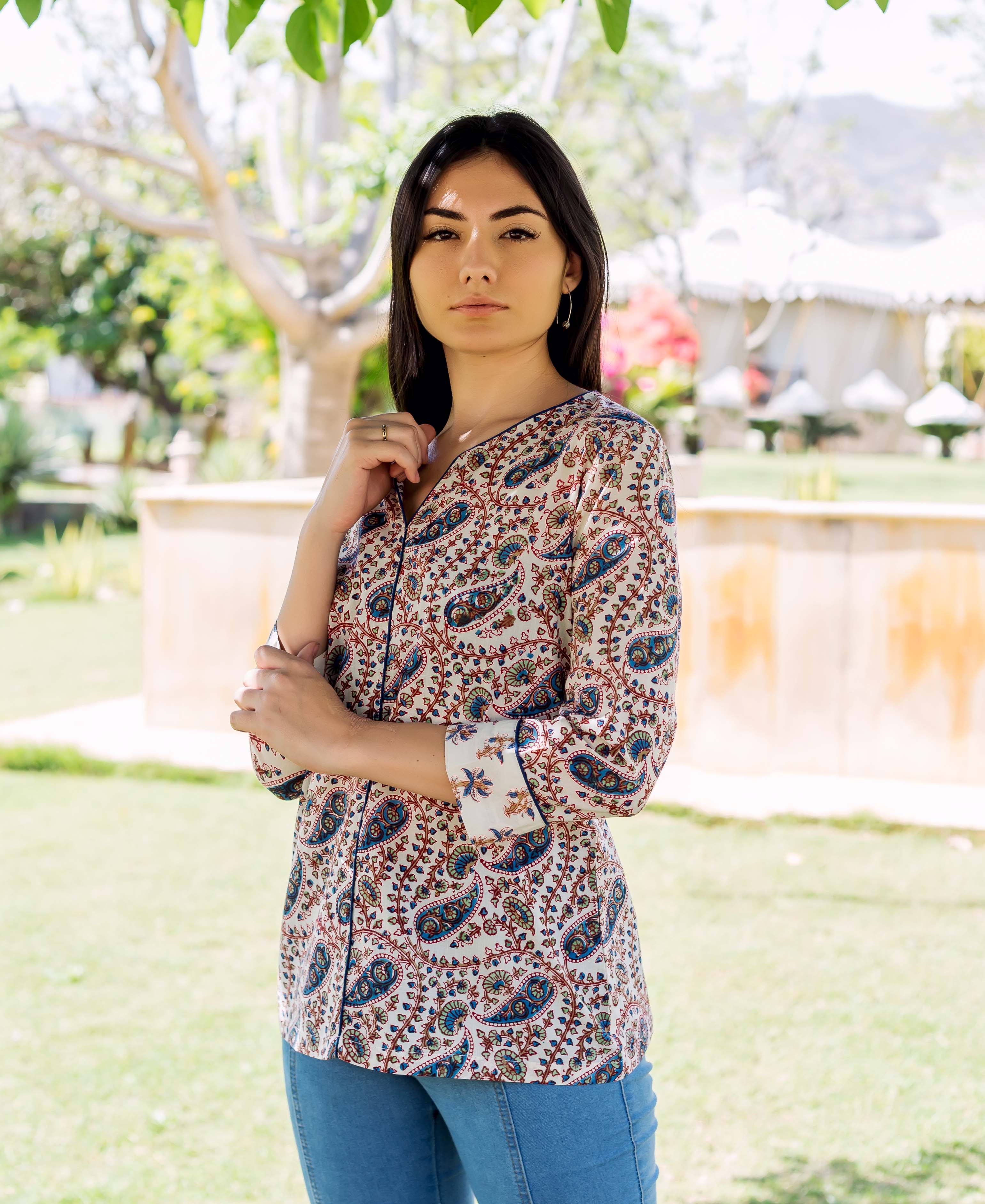 Model wearing a white button-down top with intricate blue and red paisley print outdoors.