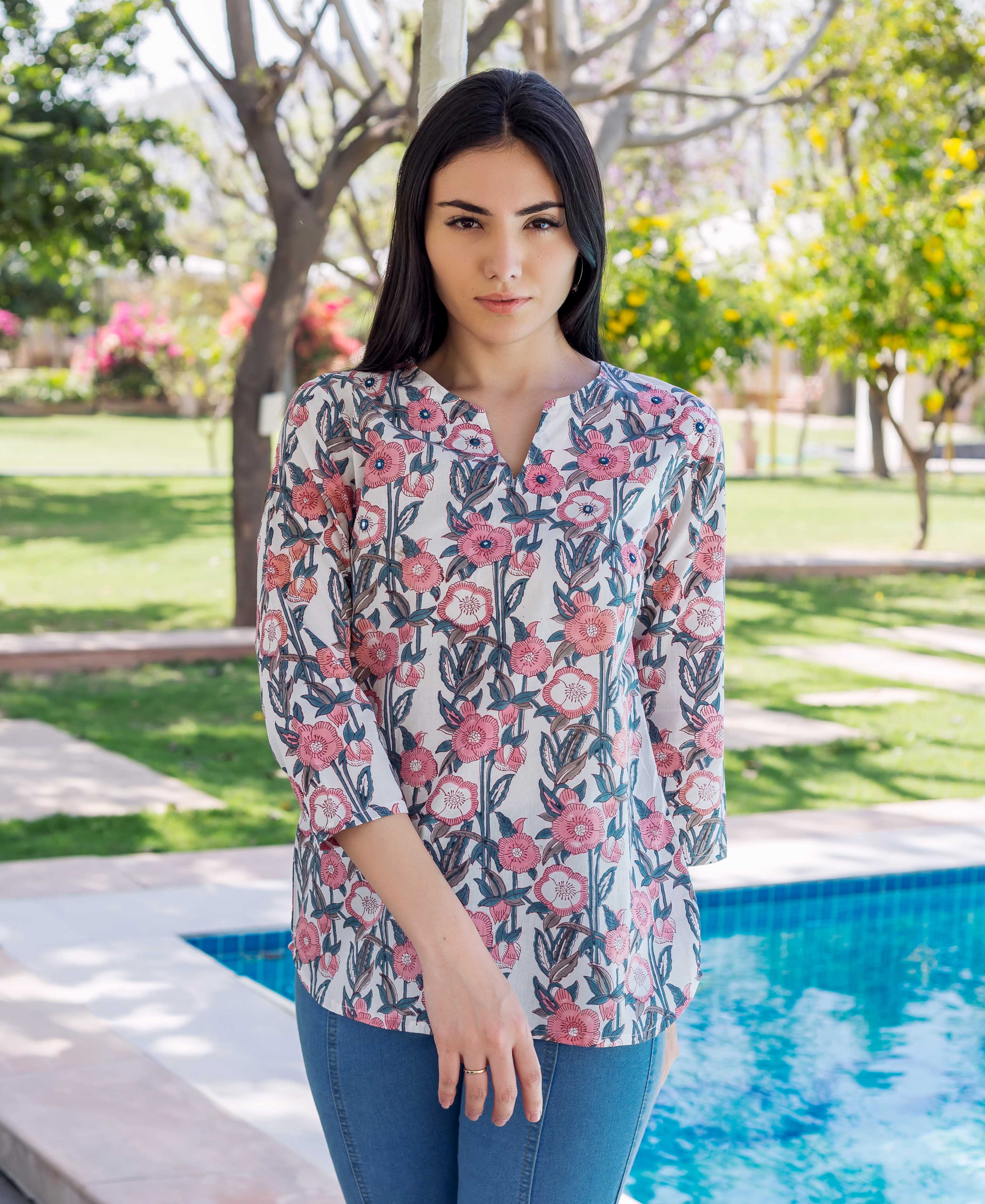 Model in white, pink, and grey block-printed floral tunic, standing by a pool.
