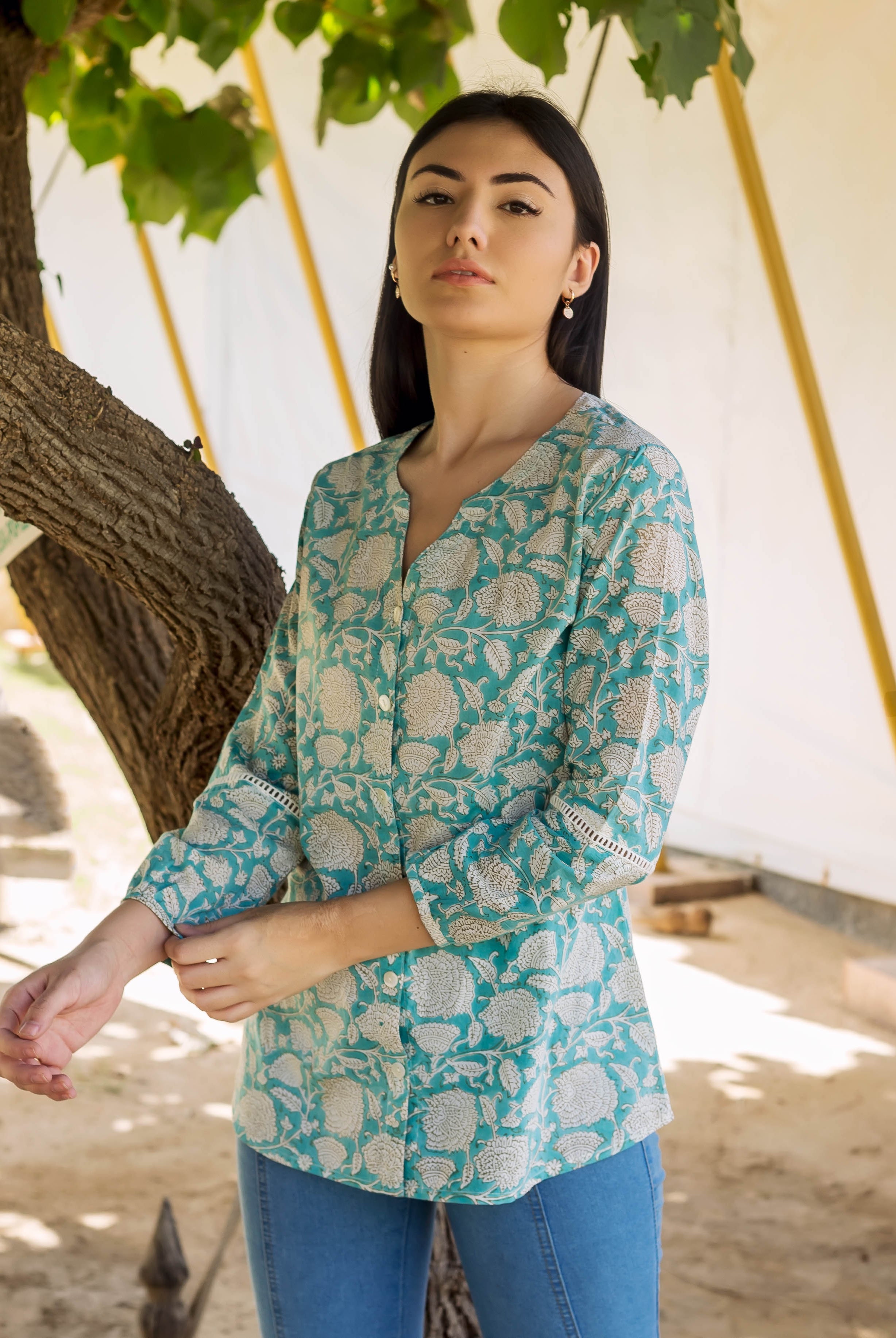 Model in teal hand-block printed button-down top with white floral print and lace cuffs.