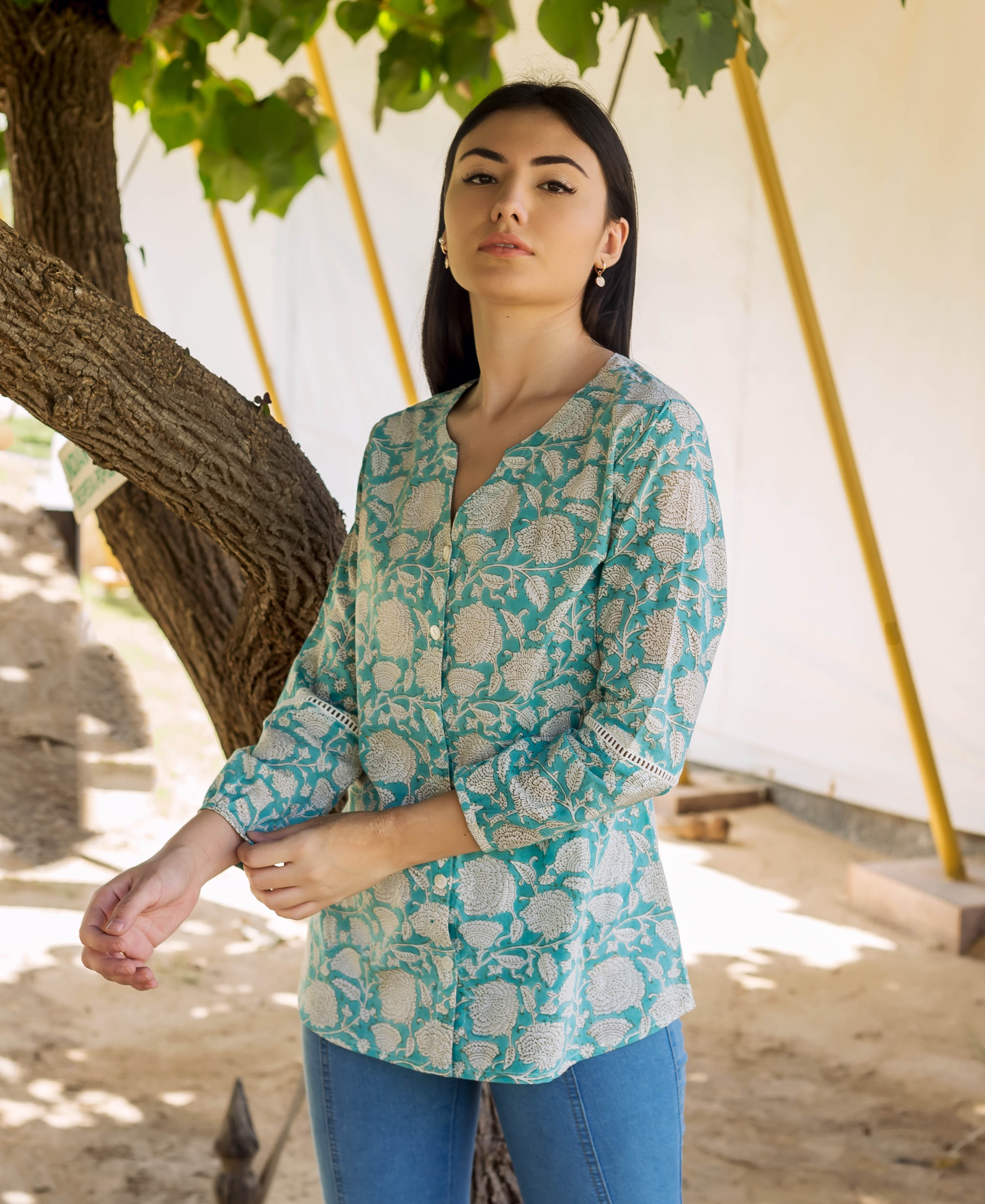 Model in teal hand-block printed button-down top with white floral print and lace cuffs.
