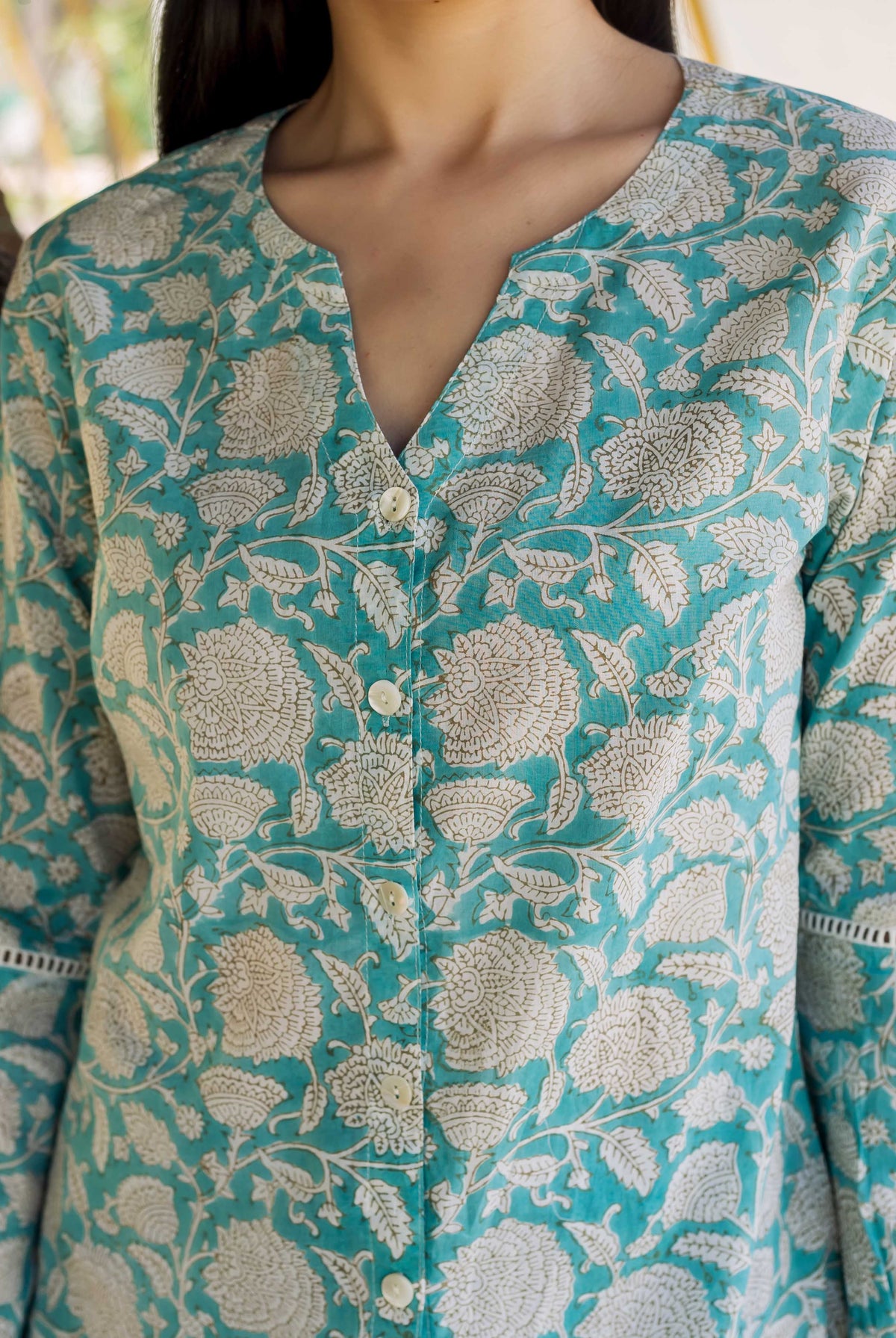 Front close-up of model wearing teal hand block printed button-down top with white florals and lace sleeves.