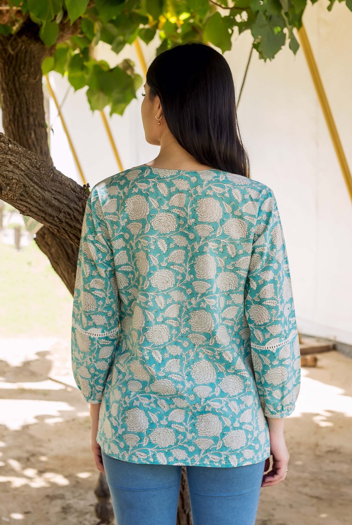 Back of model wearing teal floral print top with lace sleeves and blue bottoms.