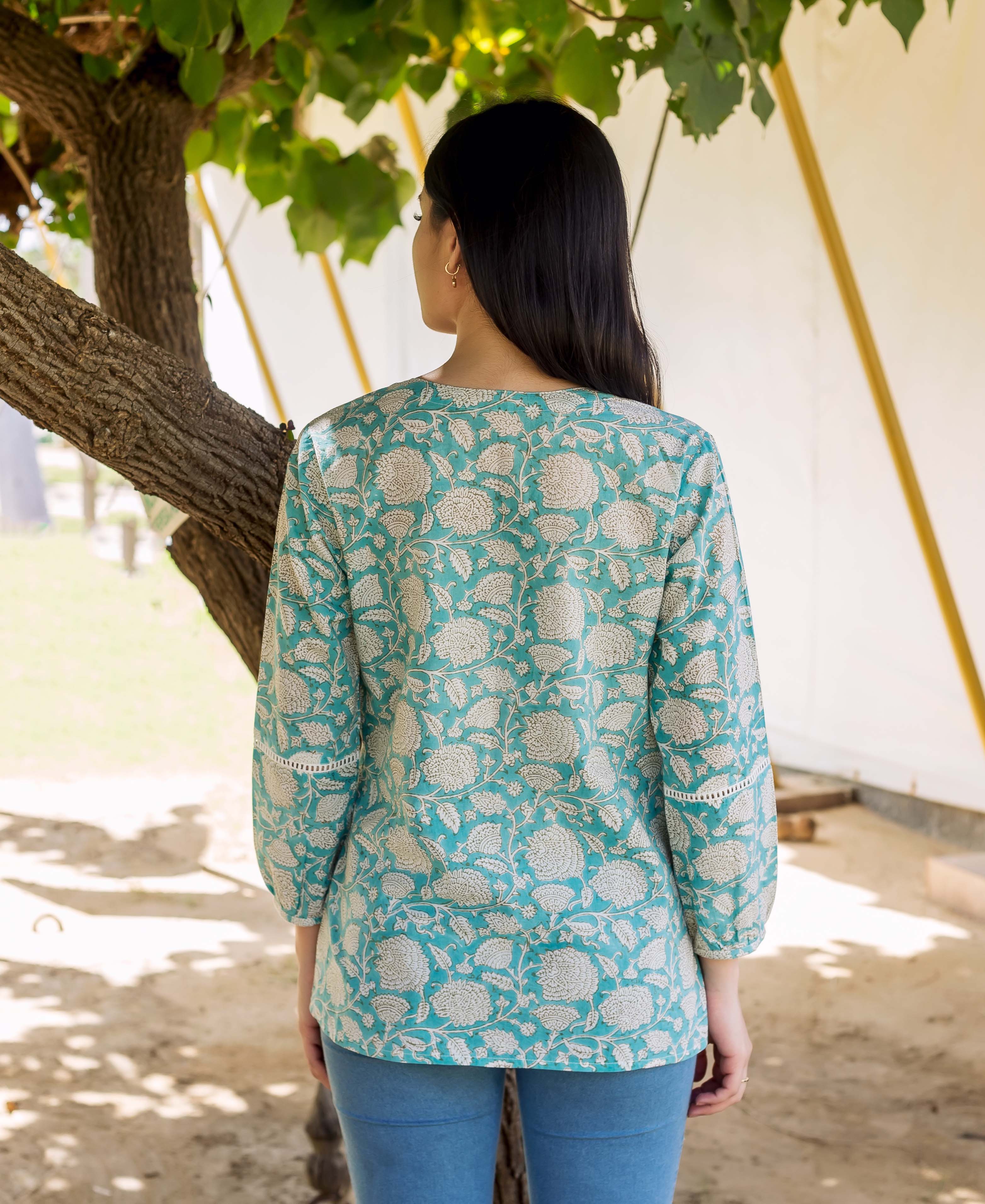 Back of model wearing teal floral print top with lace sleeves and blue bottoms.