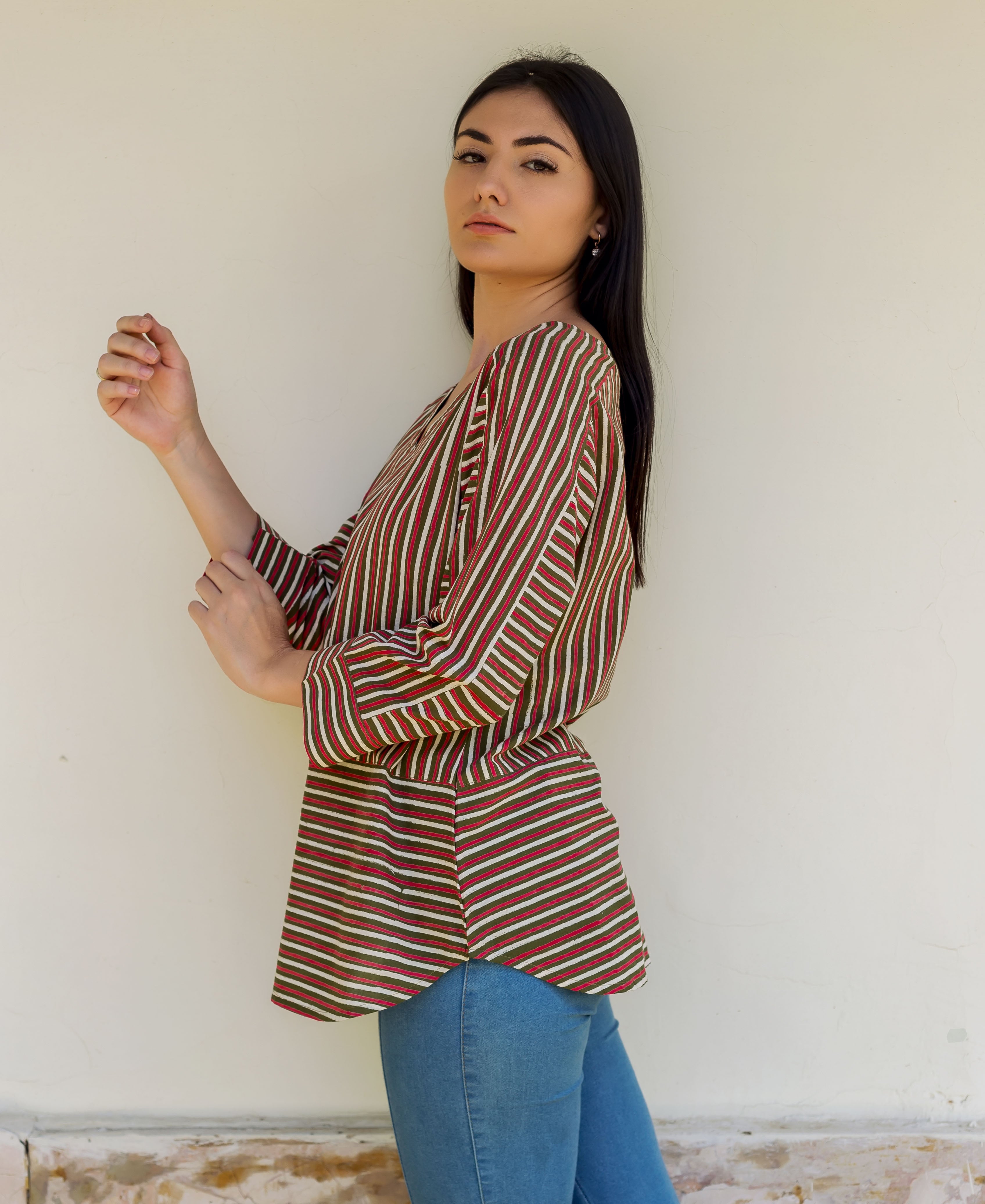 A model wearing an olive green and red striped top with a V-neckline.