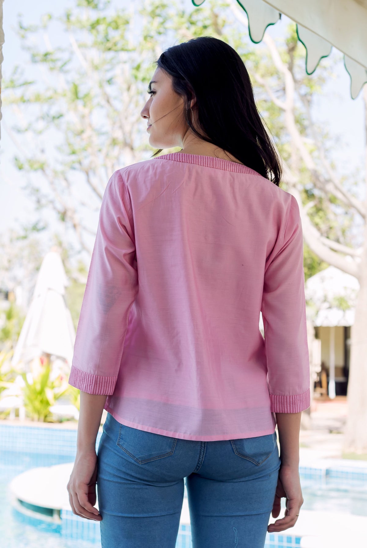 Back view of woman wearing a pink embroidered top with subtle striped neckline and cuffs.