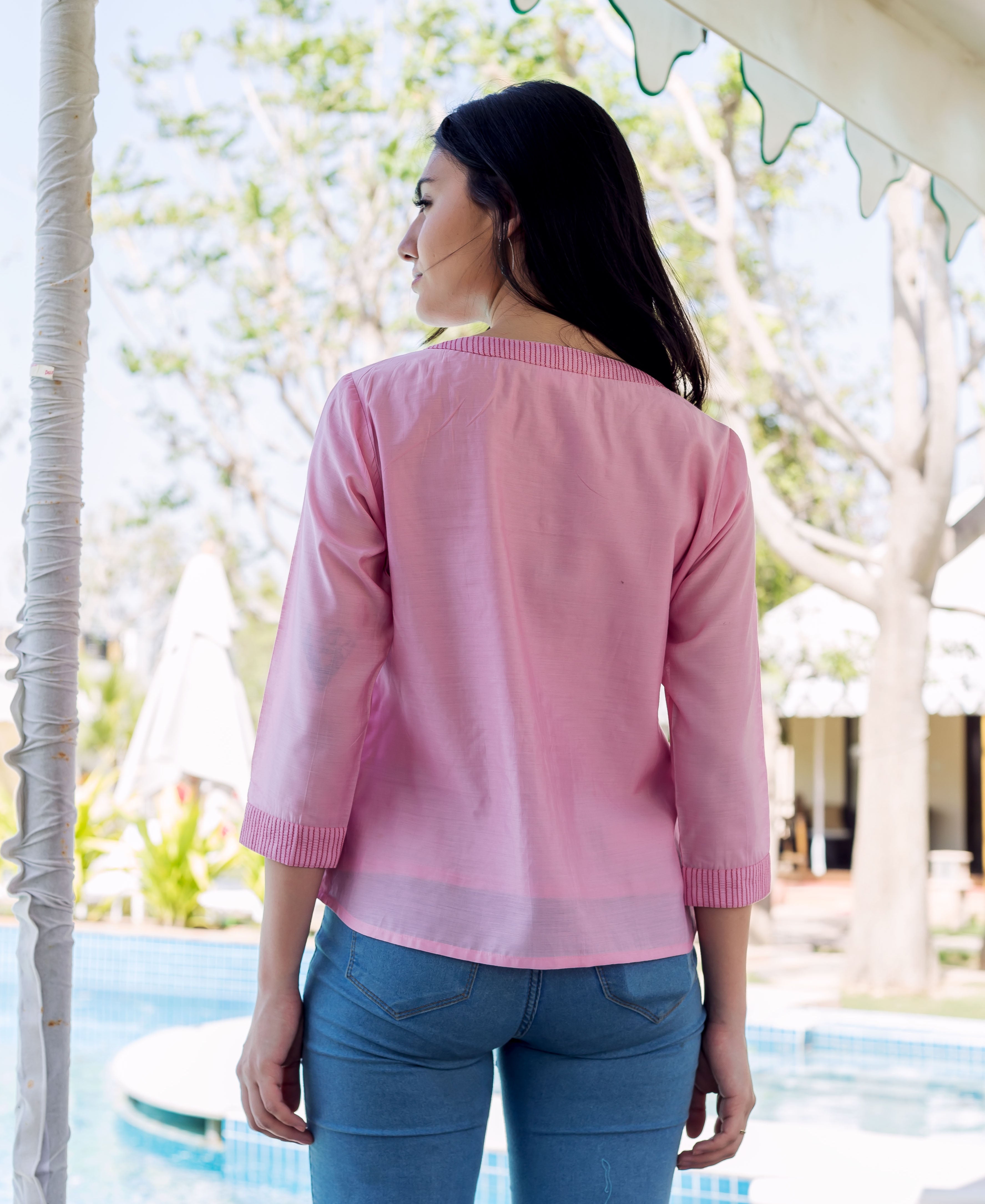 Back view of woman wearing a pink embroidered top with subtle striped neckline and cuffs.
