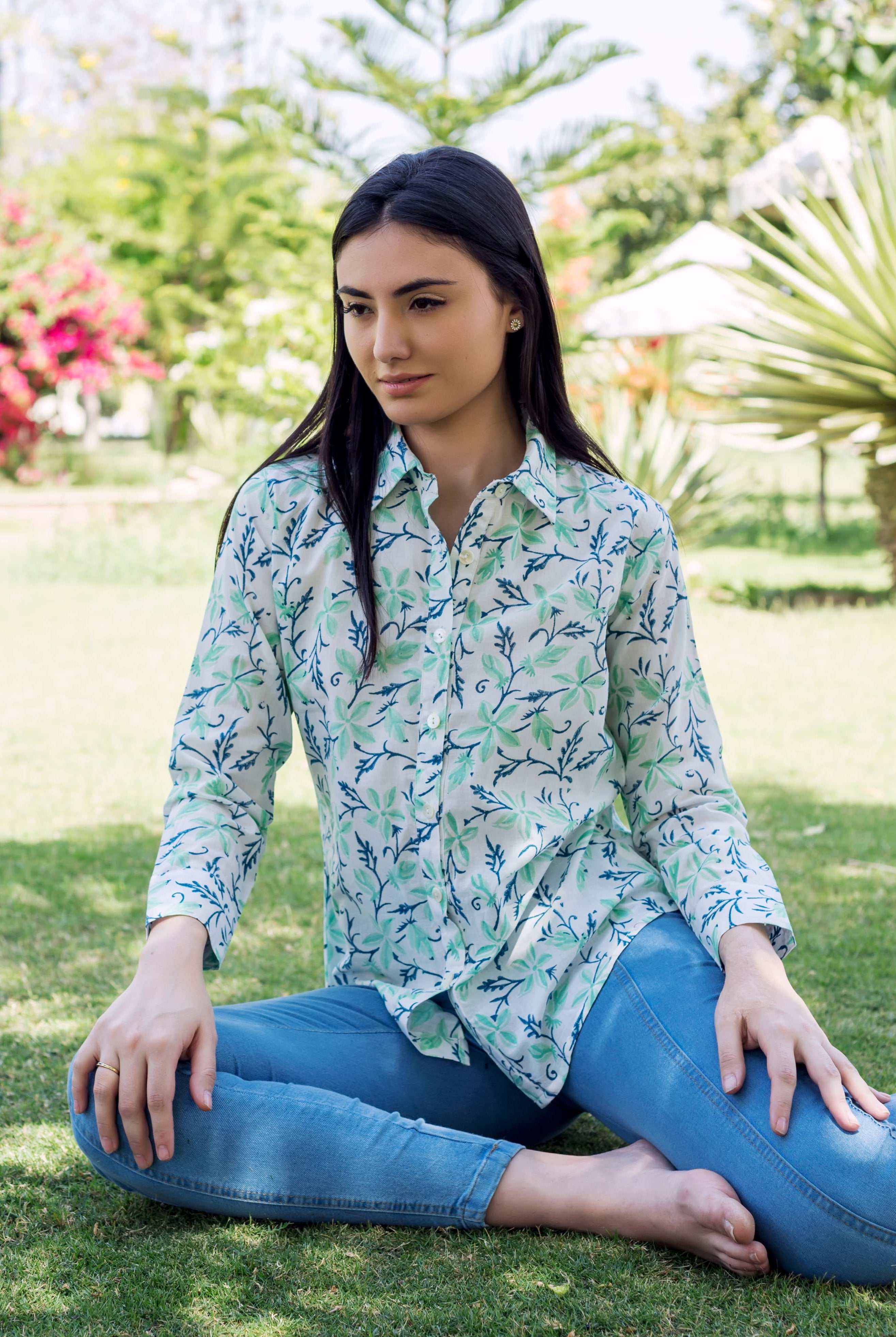 Woman in sea green and blue block printed leafy pattern shirt, sitting on grass.