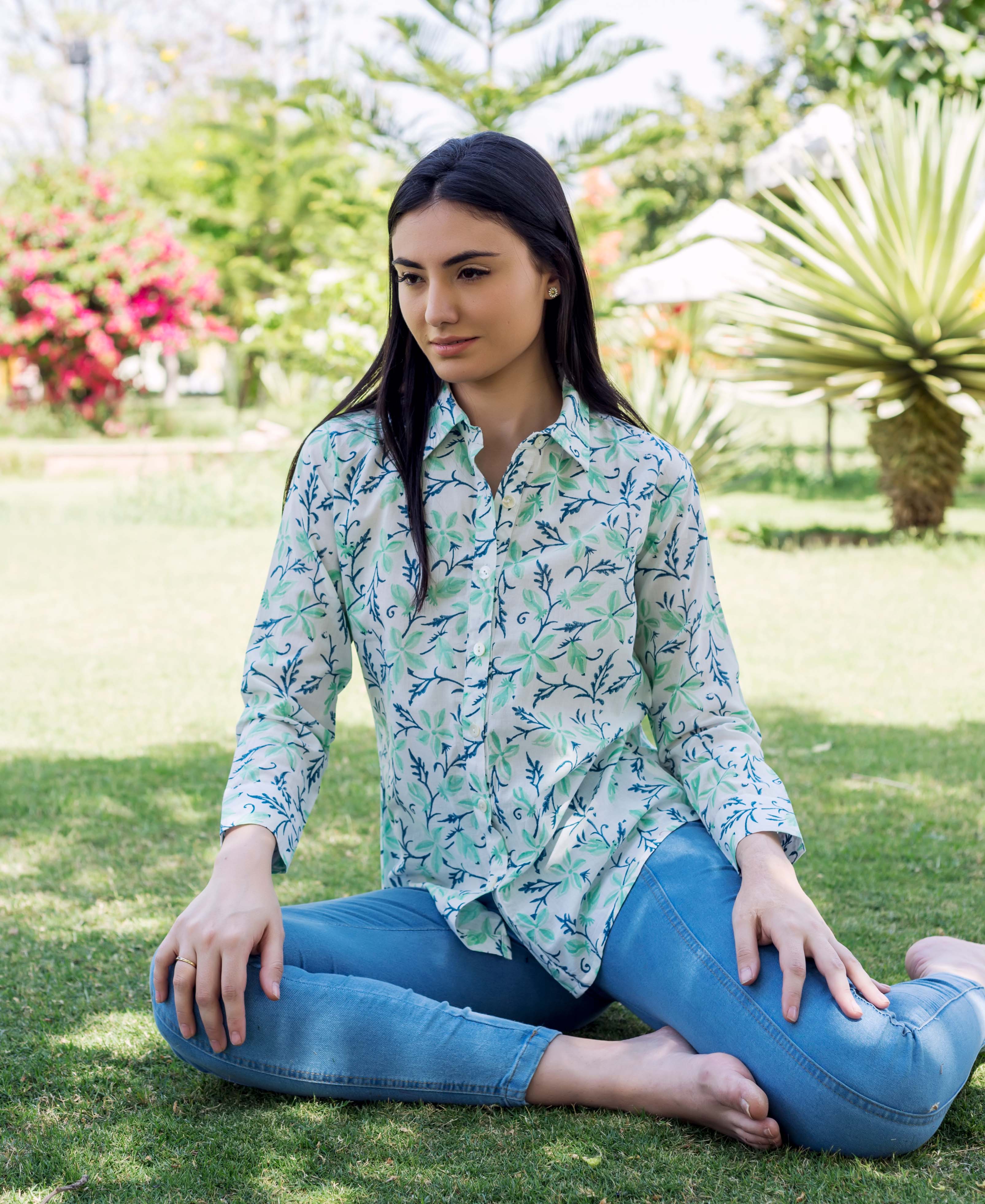 Woman in sea green and blue block printed leafy pattern shirt, sitting on grass.