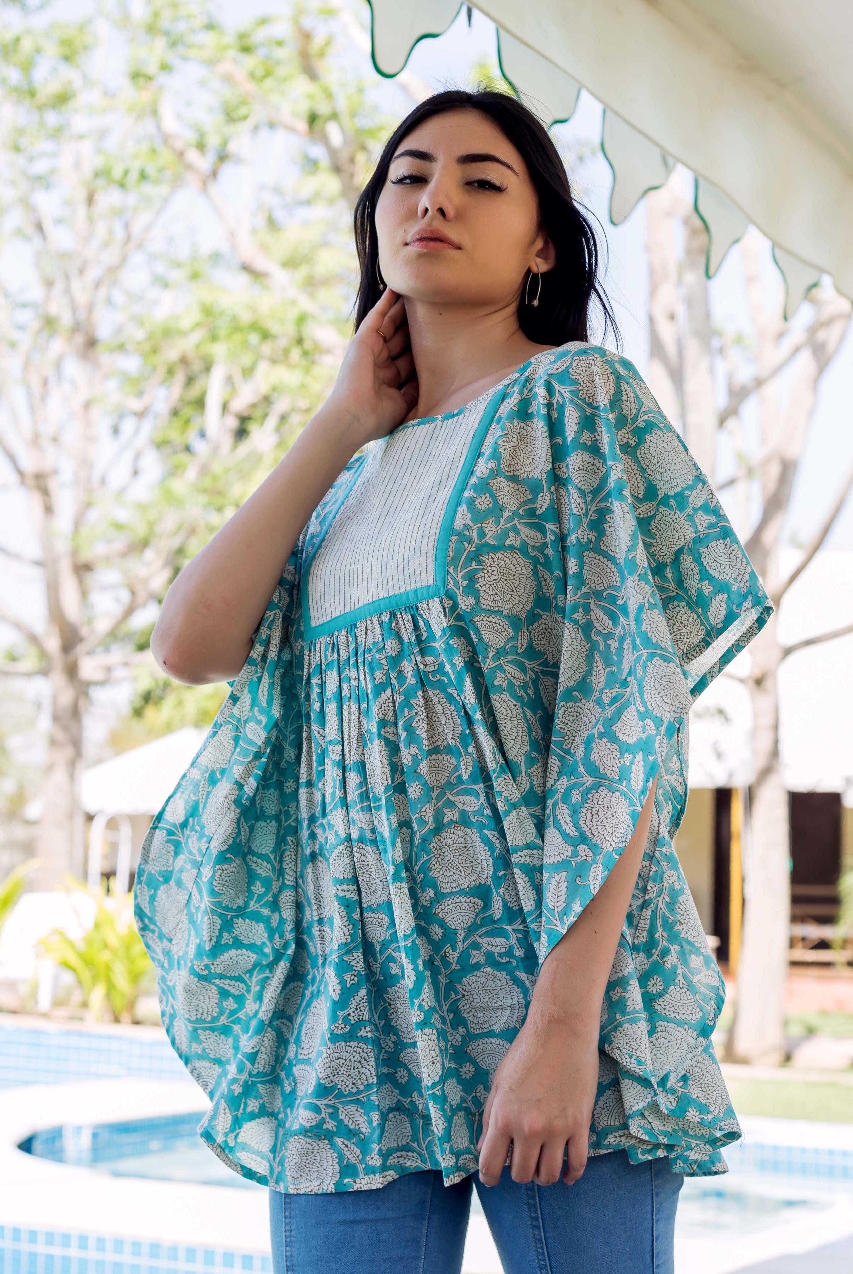 Woman models sea blue floral printed kaftan top with white pleated yoke over blue jeans.