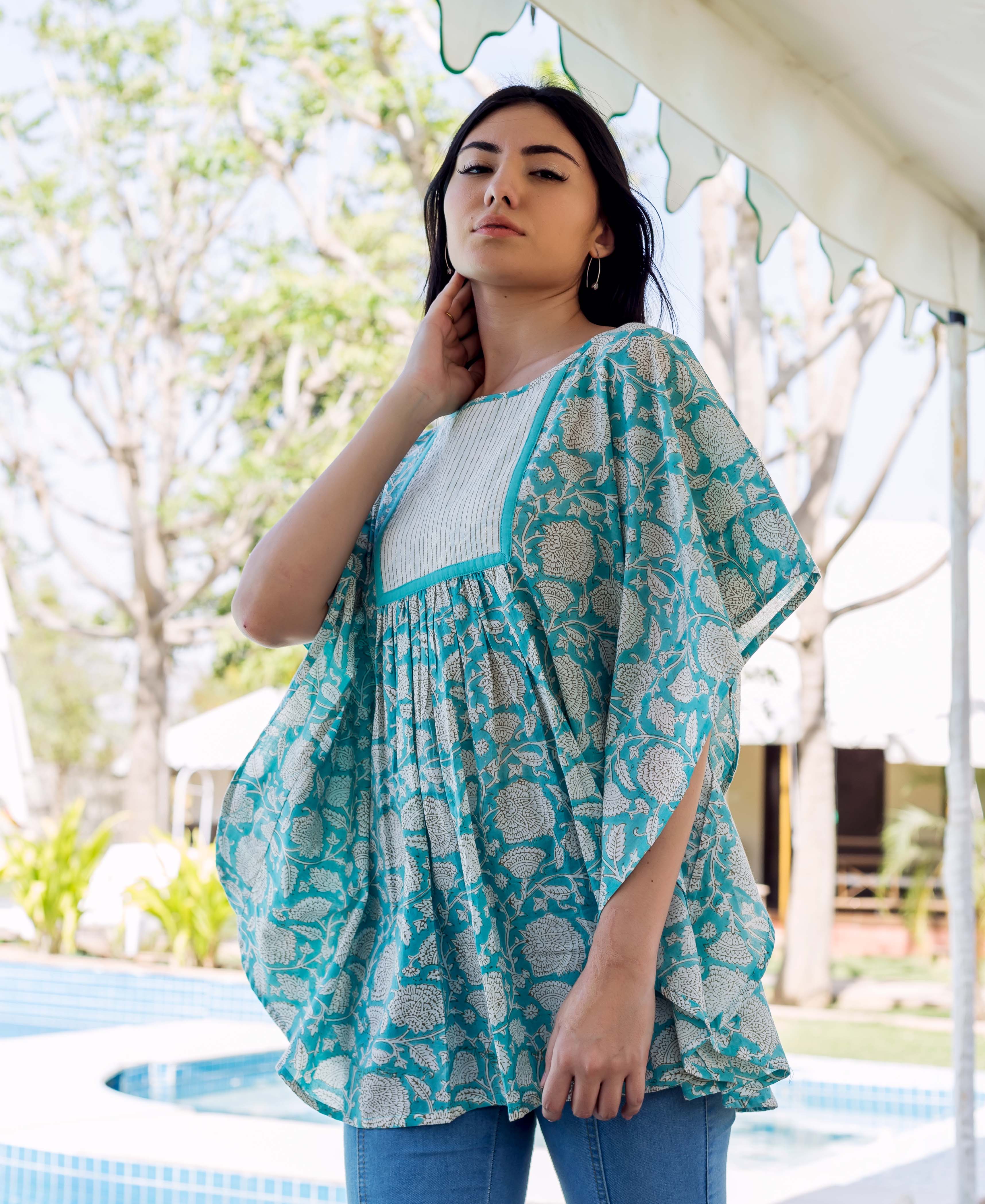 Woman models sea blue floral printed kaftan top with white pleated yoke over blue jeans.