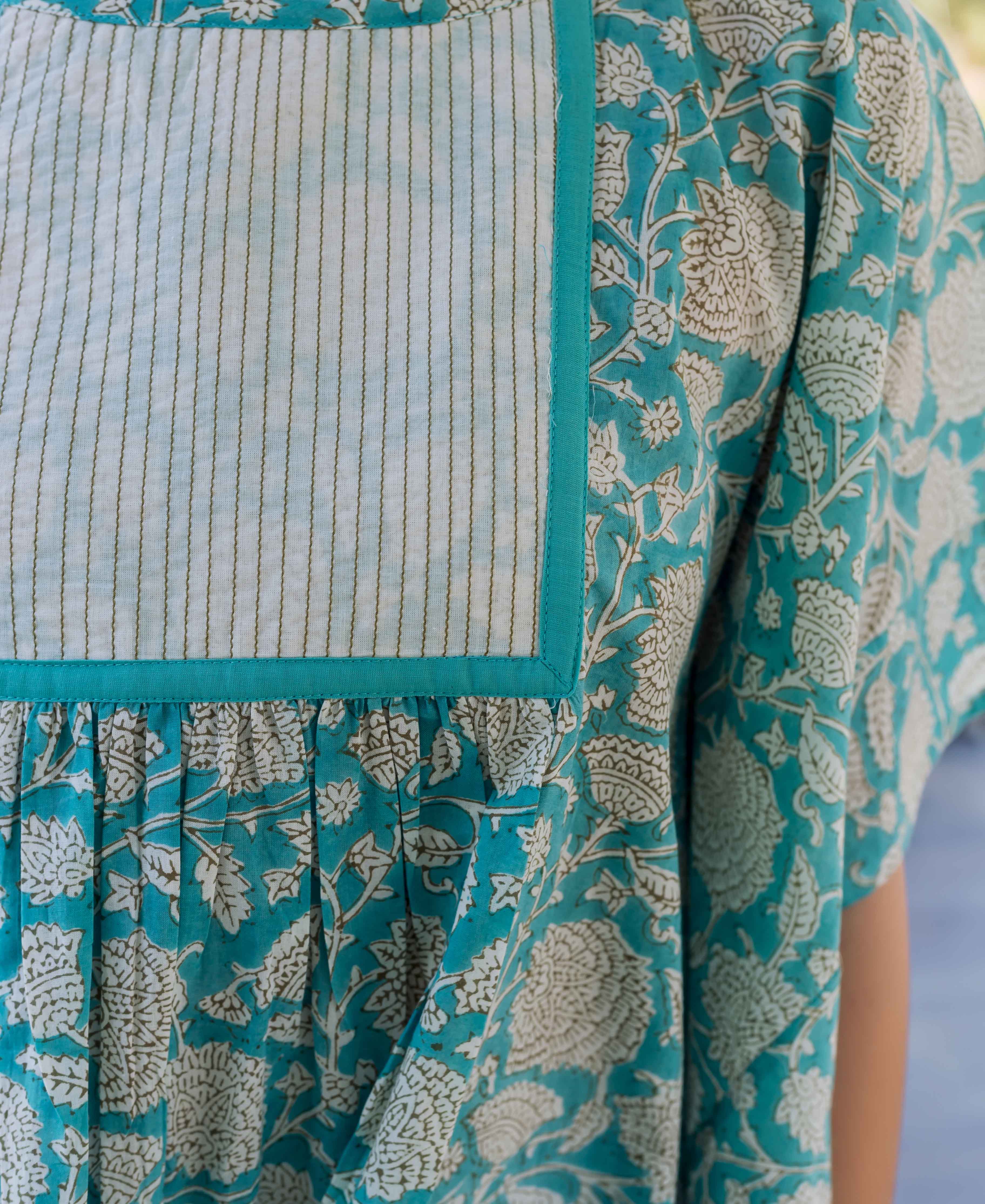 Close-up of a sea blue floral kaftan top with a striped yoke and gathered fabric.