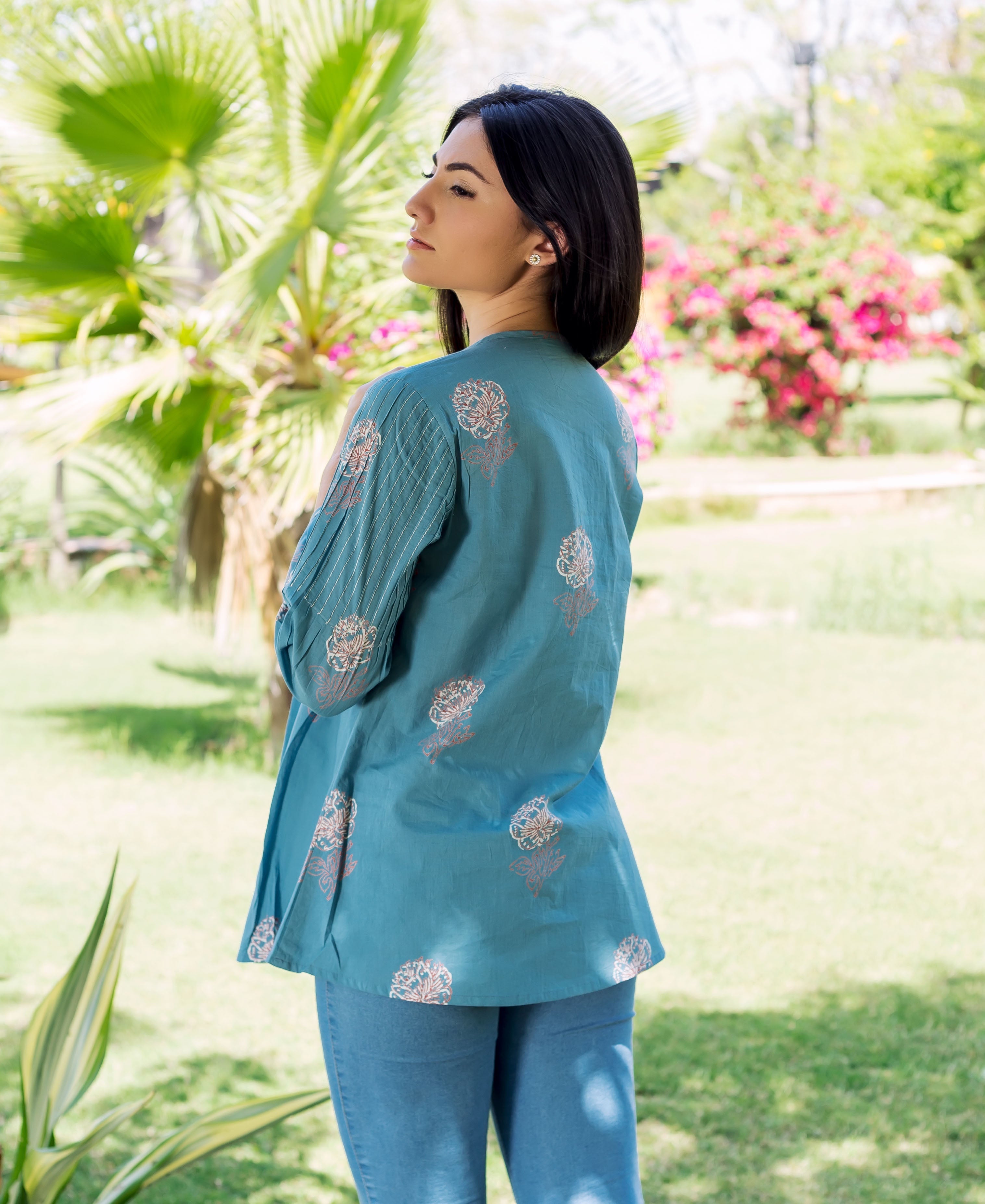 Model wears stone blue top with hand-block printed flowers and pleated statement sleeve, back view.