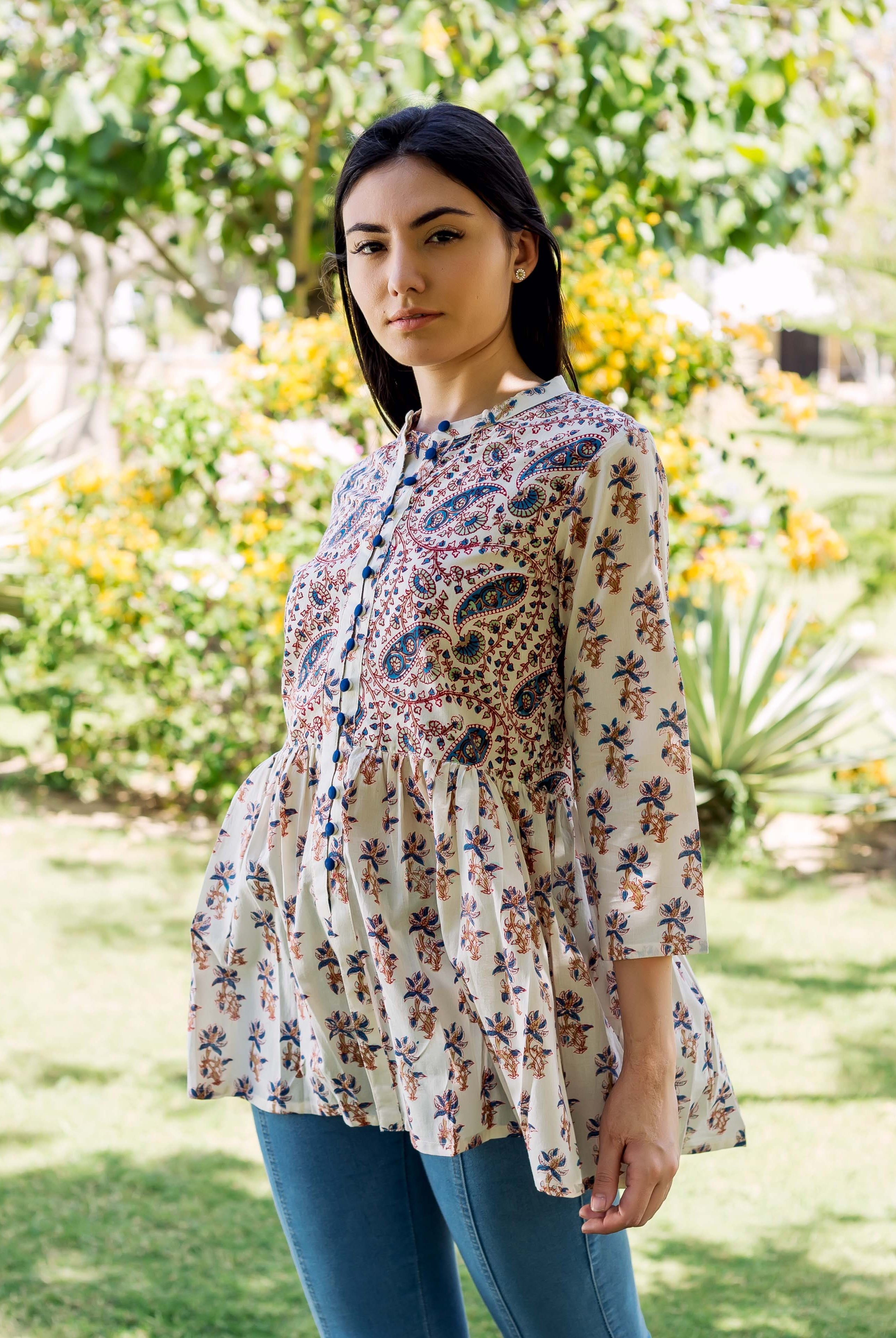 Young woman models white peplum top with blue and brown ethnic hand-block prints in a garden.