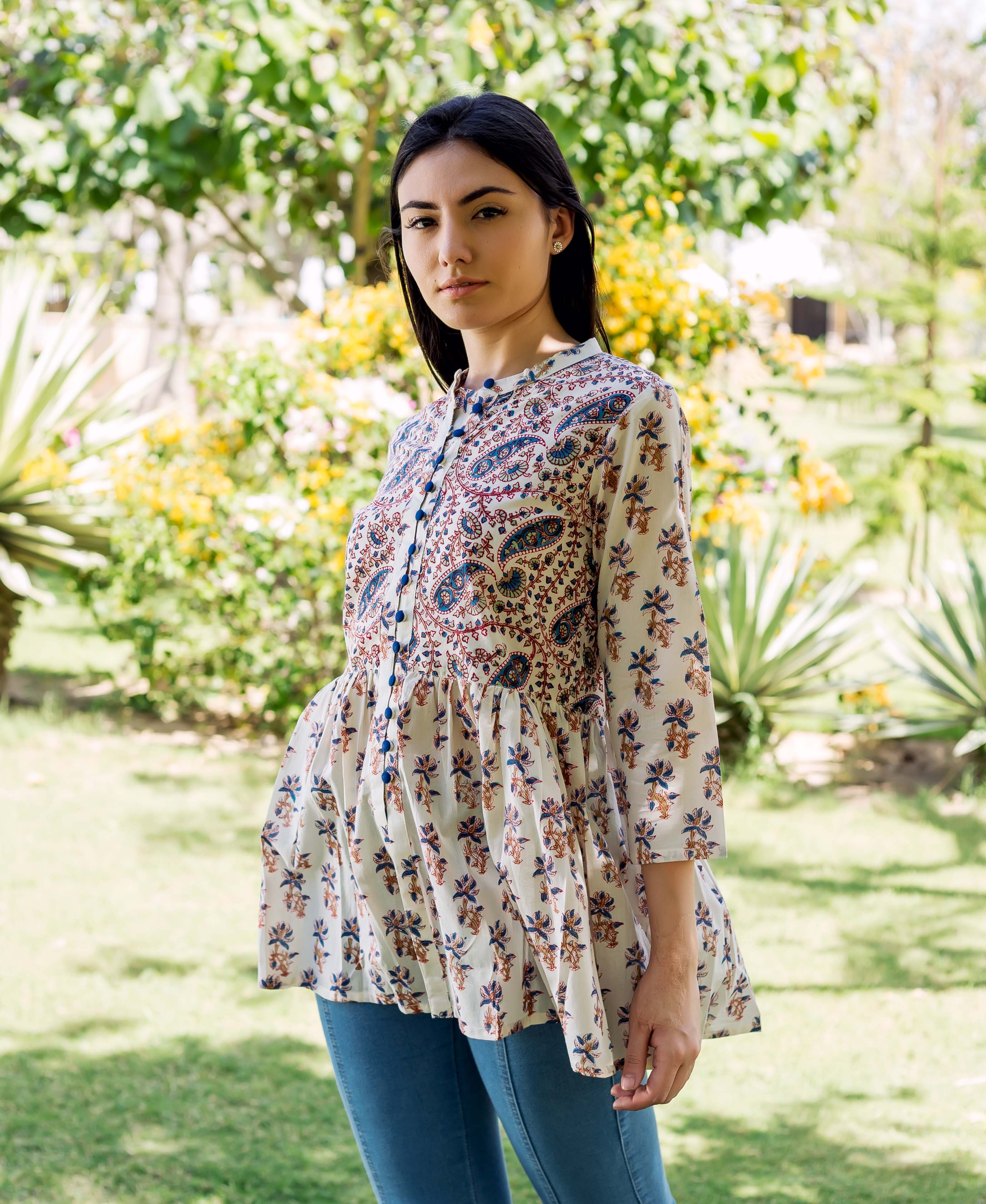 Young woman models white peplum top with blue and brown ethnic hand-block prints in a garden.