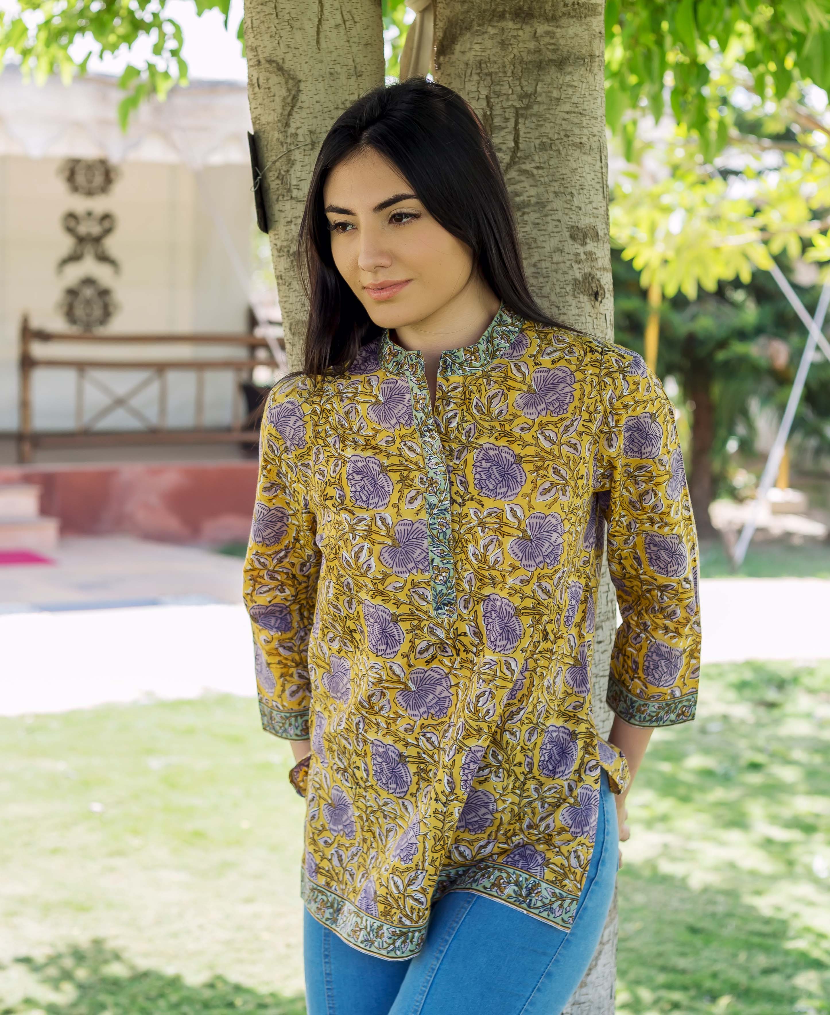 Woman wearing a yellow hand block printed tunic with purple florals, mandarin collar, leaning on a tree.