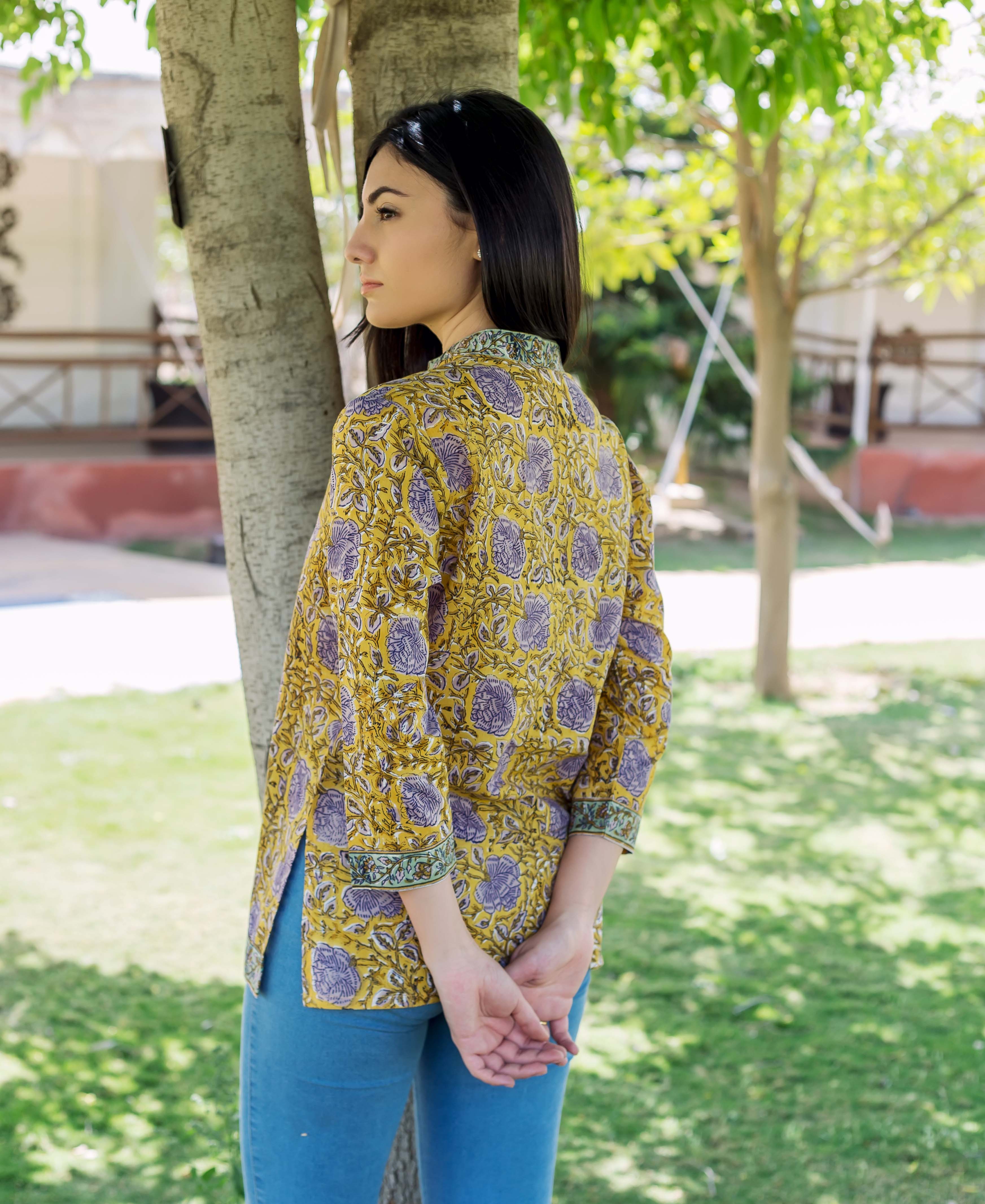 Woman wearing yellow hand block printed top with purple floral design, back view.