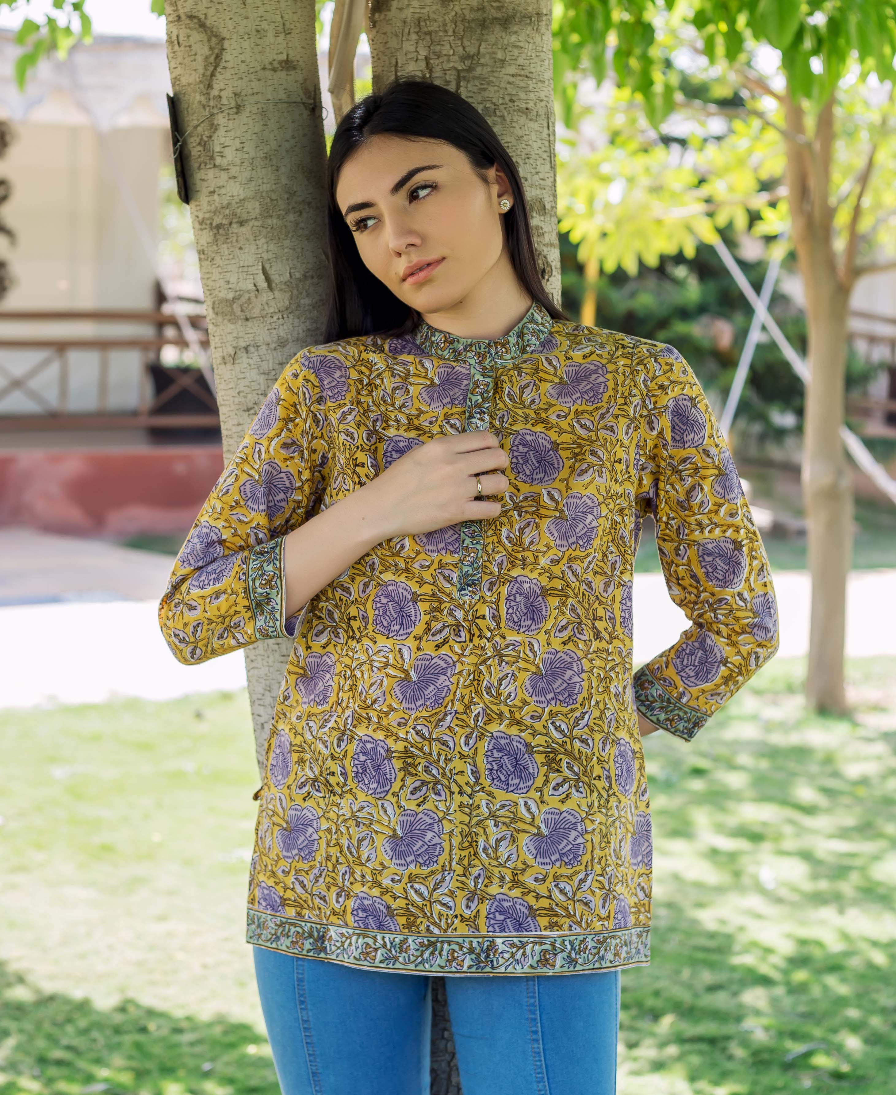 Woman wearing a yellow and grey hand block printed floral top, leaning against a tree.